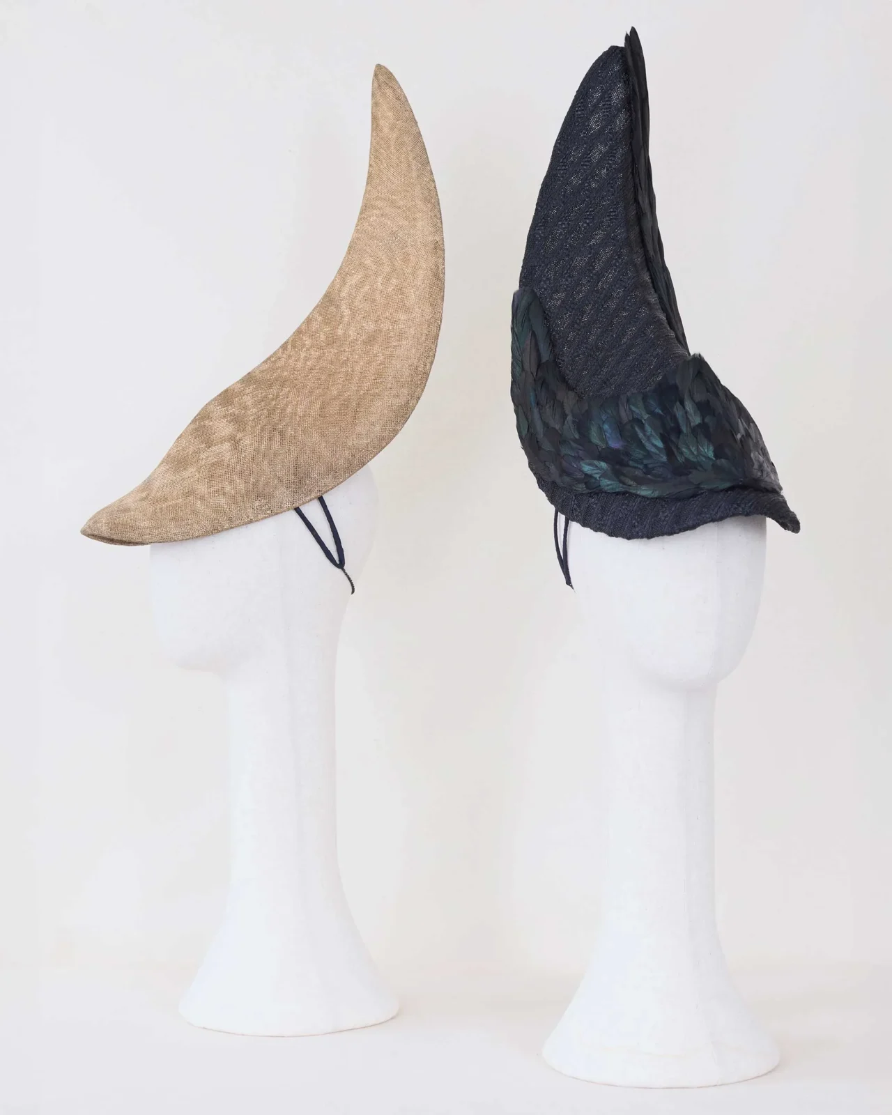 Display of fashion hats on white mannequin heads: two checkered berets (black‑white and white‑red), a black brimless cap, a gray tweed cap, and two tall pointed witch hats (beige and black).