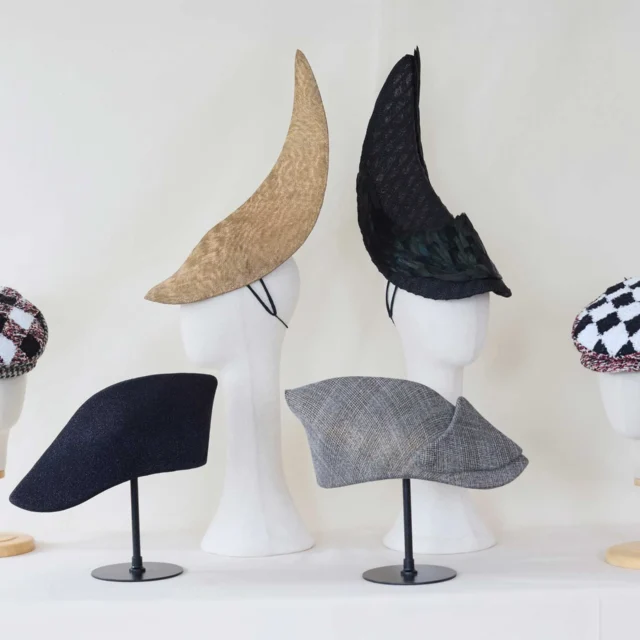 Several fabric hats displayed on white mannequin heads with different textures and patterns (beige, black, tweed, and checkered).