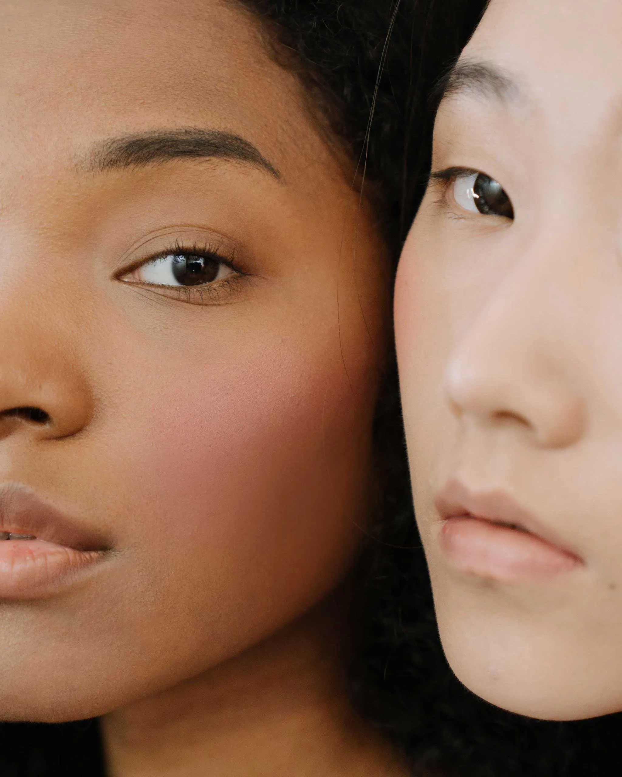 Close-up of two people with cheeks touching; the dark-skinned person's eye and mouth are visible on the left, with the lighter-skinned person's face partly on the right.