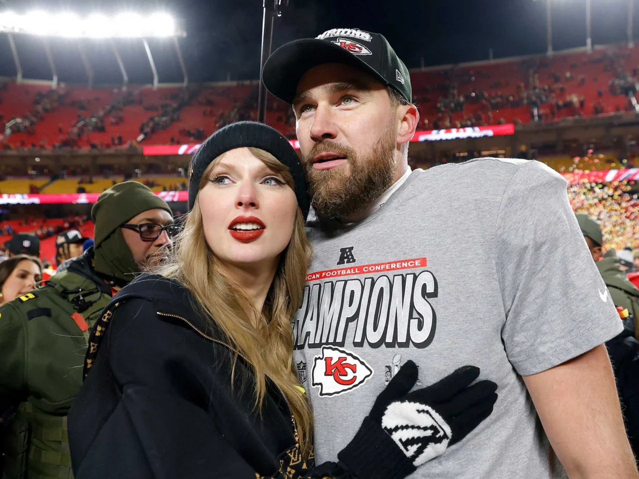 Couple posing for a selfie on a football field after a Kansas City Chiefs win, stadium lights glowing behind them.