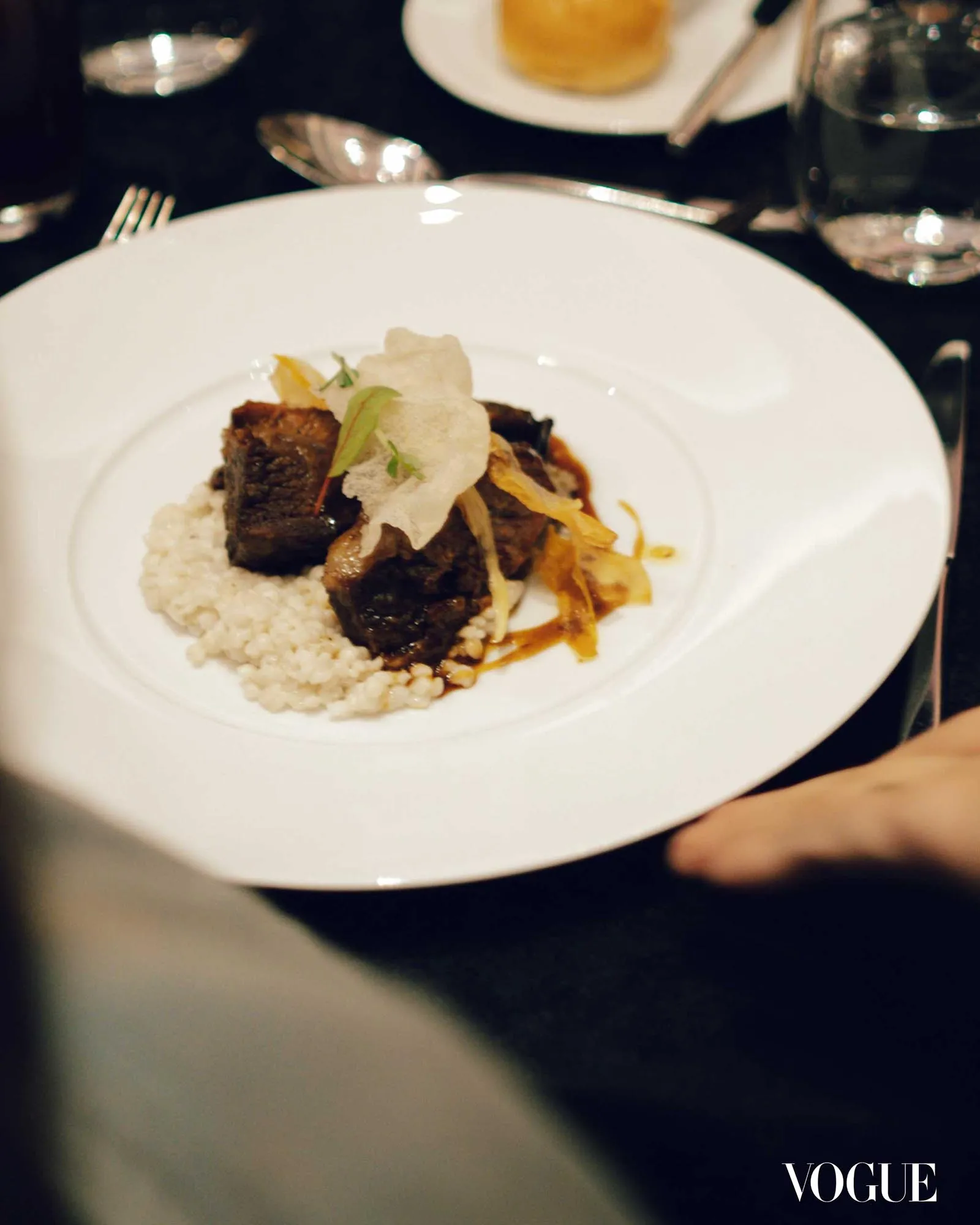 Plate with braised beef over rice and crispy garnish on a dark table.