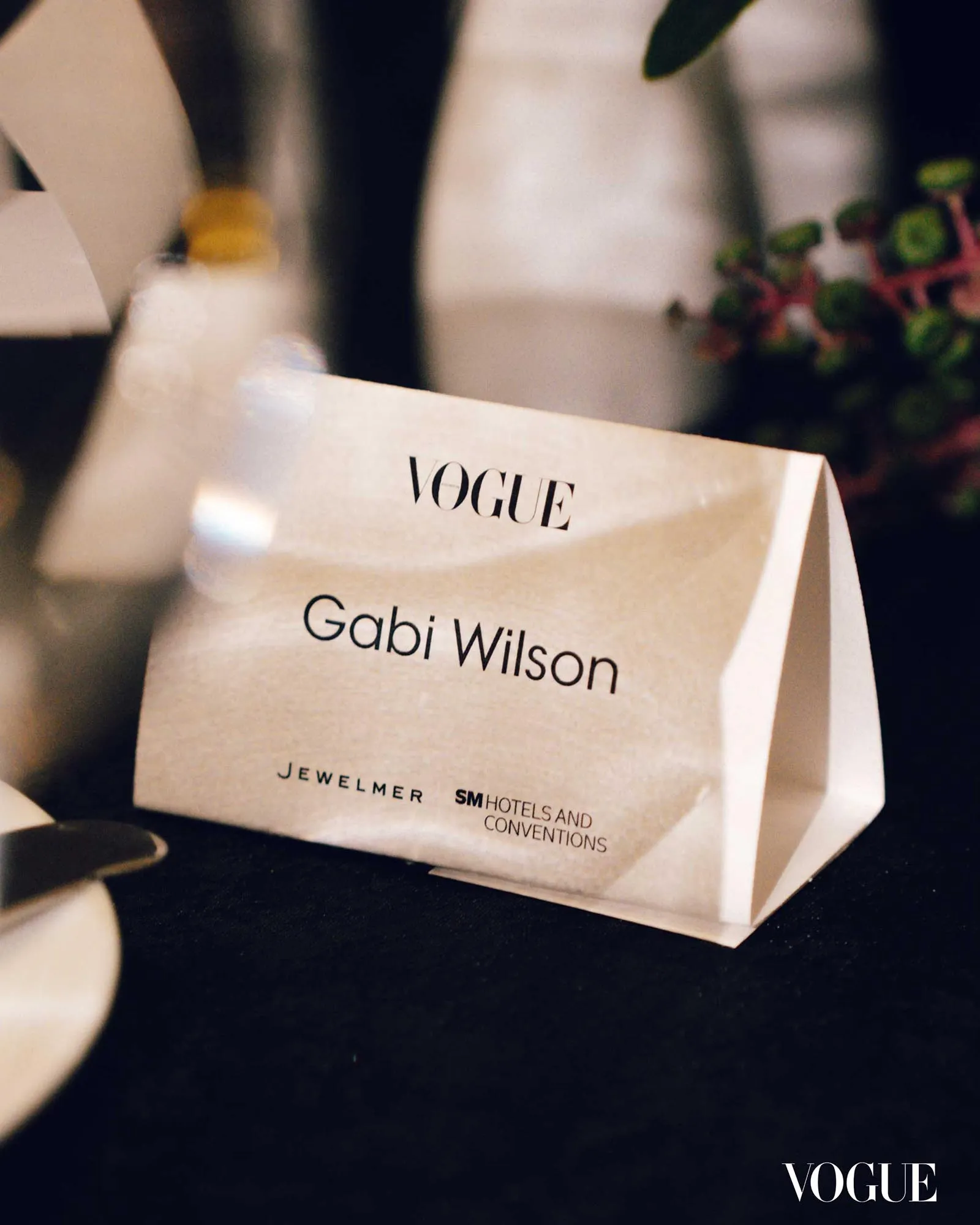 White Vogue shopping bag with the name 'Gabi Wilson' printed on it, resting on a dark surface.