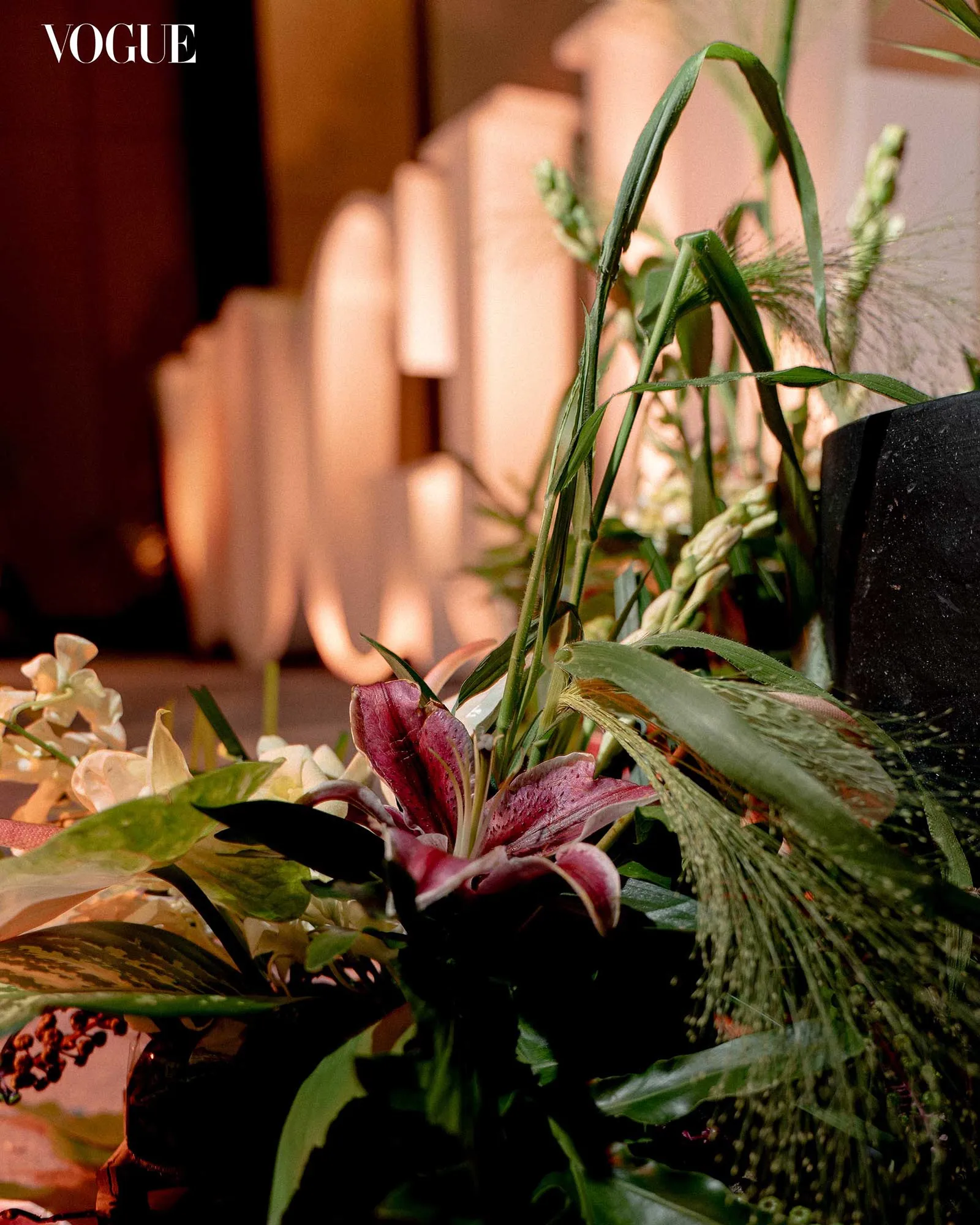 Close-up of a floral arrangement with green leaves and pink and cream flowers, Vogue logo in the upper left corner.