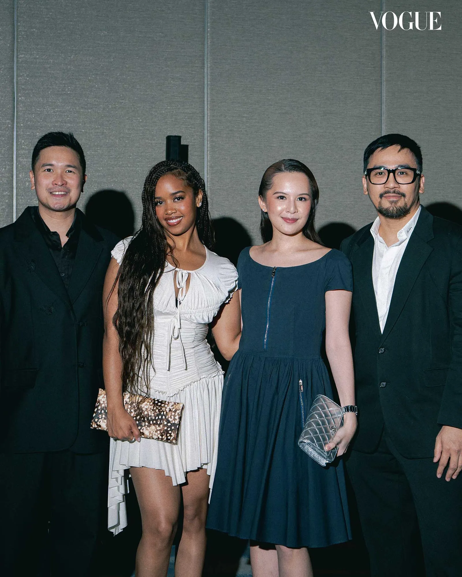 Four people in formal attire posing together with the Vogue logo in the top-right corner.