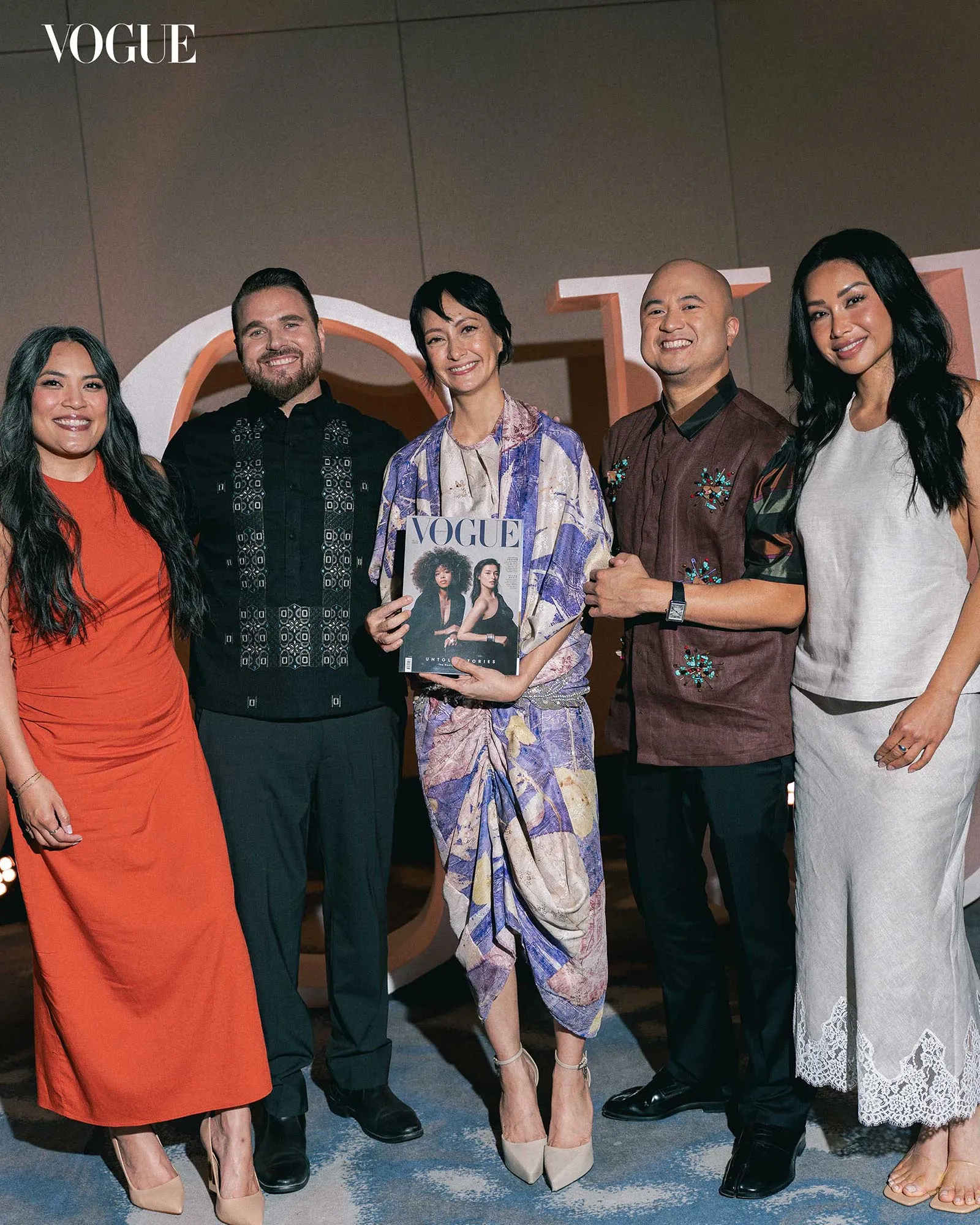 Five people pose together at a Vogue event; the center person holds a Vogue magazine cover.