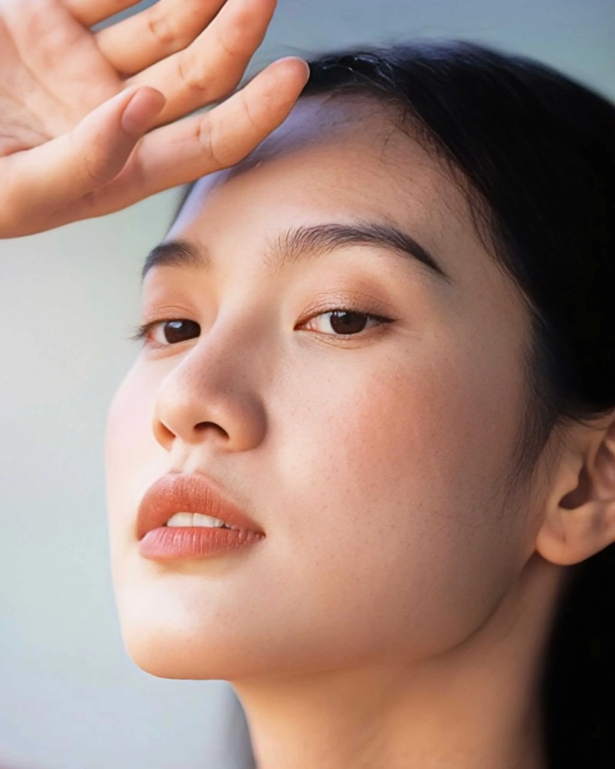 Close-up of a person’s face with a hand resting on the forehead, looking to the side.