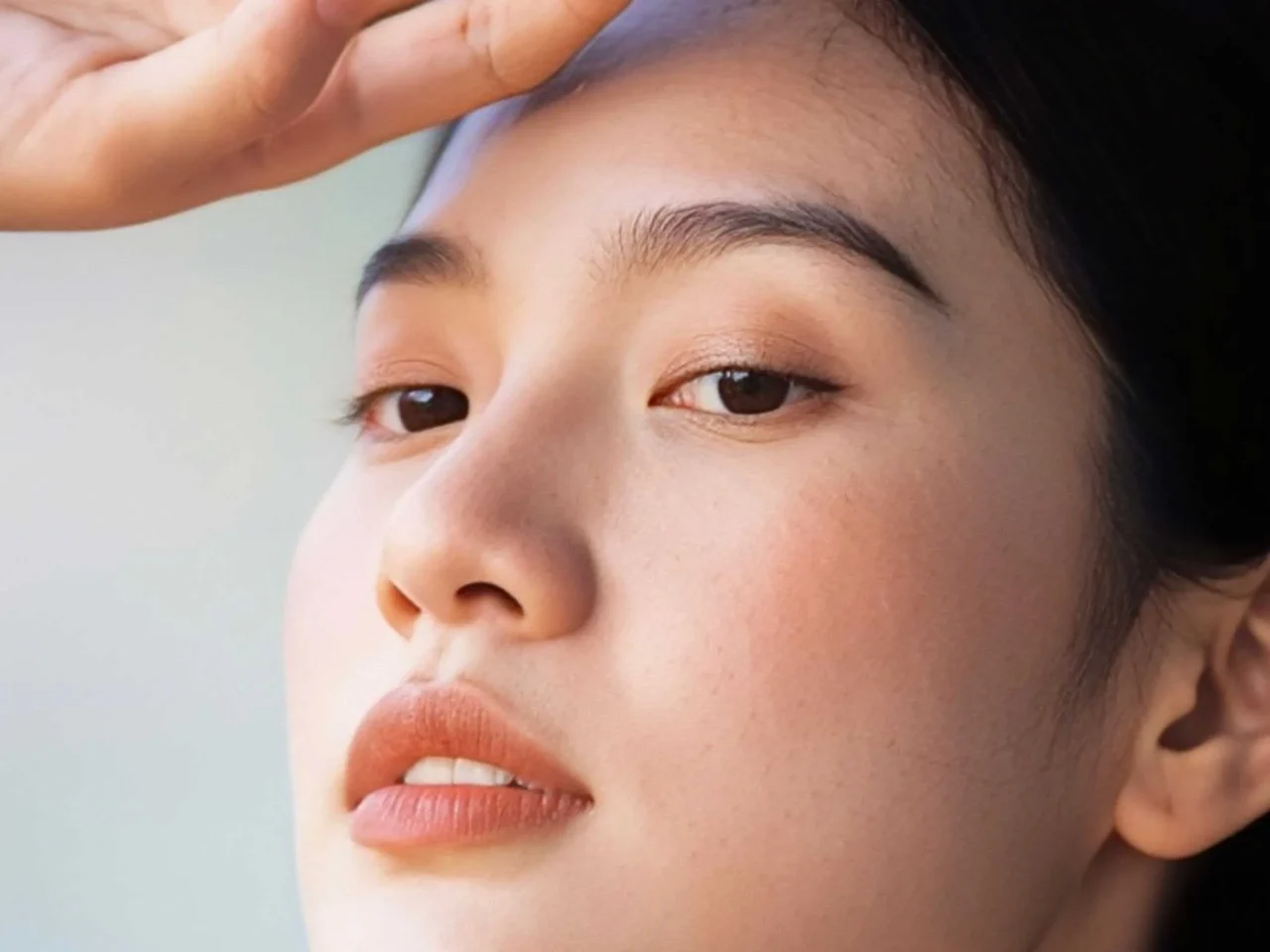 Close-up of a woman's half-face with peach makeup, focusing on lips and nose.