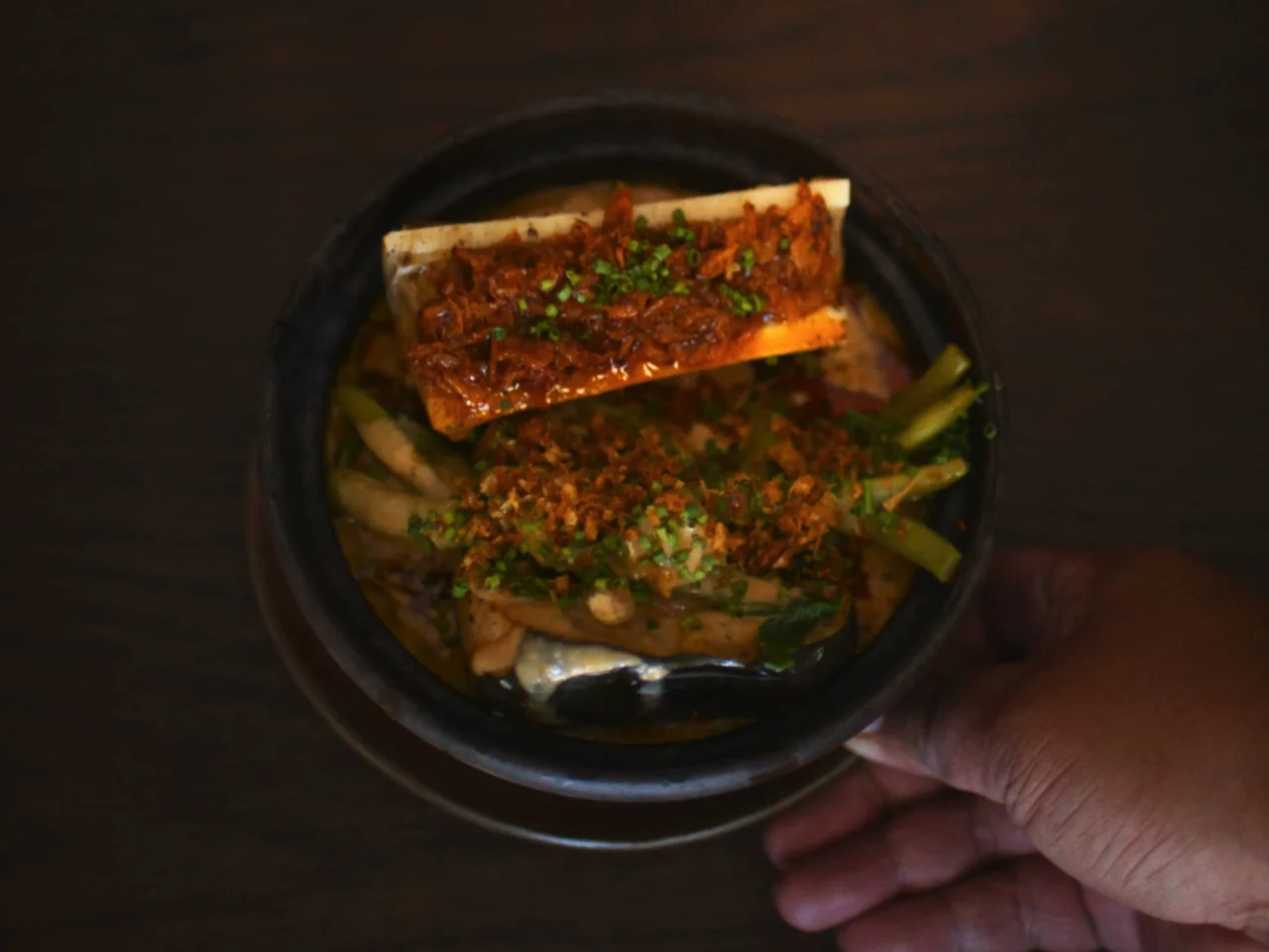 Two hands hold a cluster of small round bread rolls with a crusty, sesame-speckled surface.