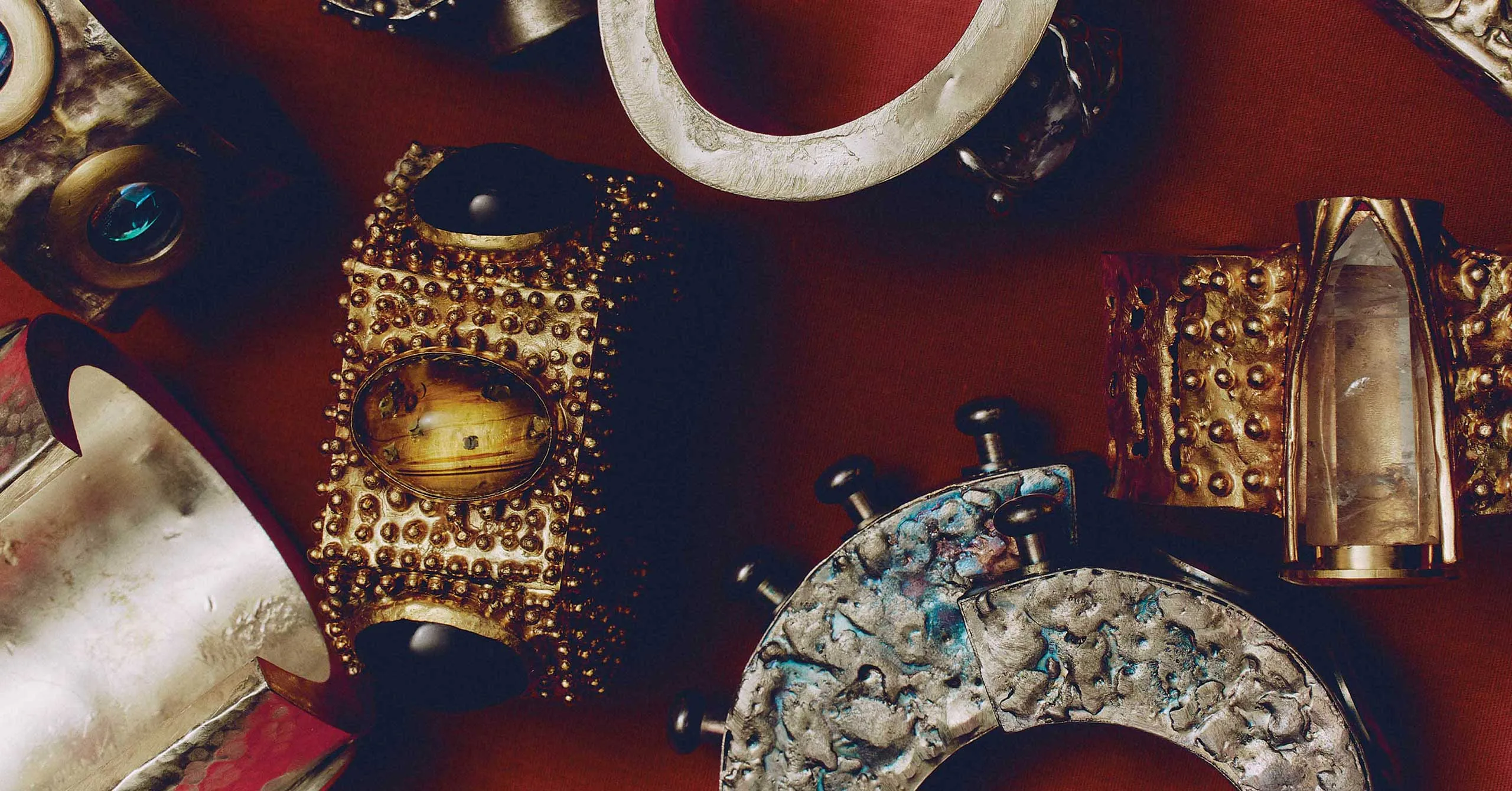 Close-up of antique metal armor pieces with riveted studs on a dark red background.