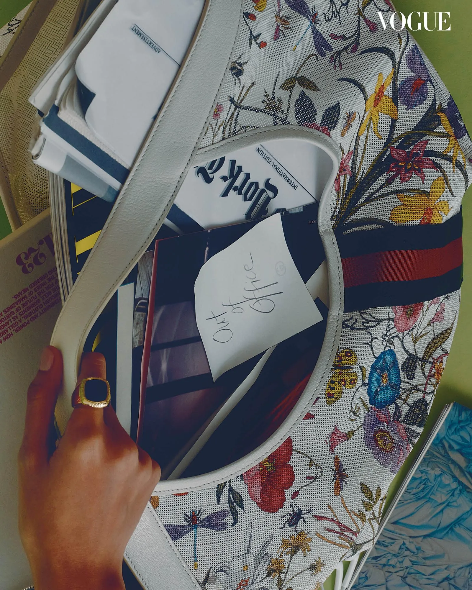 Close-up of a floral-patterned bag with papers inside and a hand with a gold ring touching the strap.