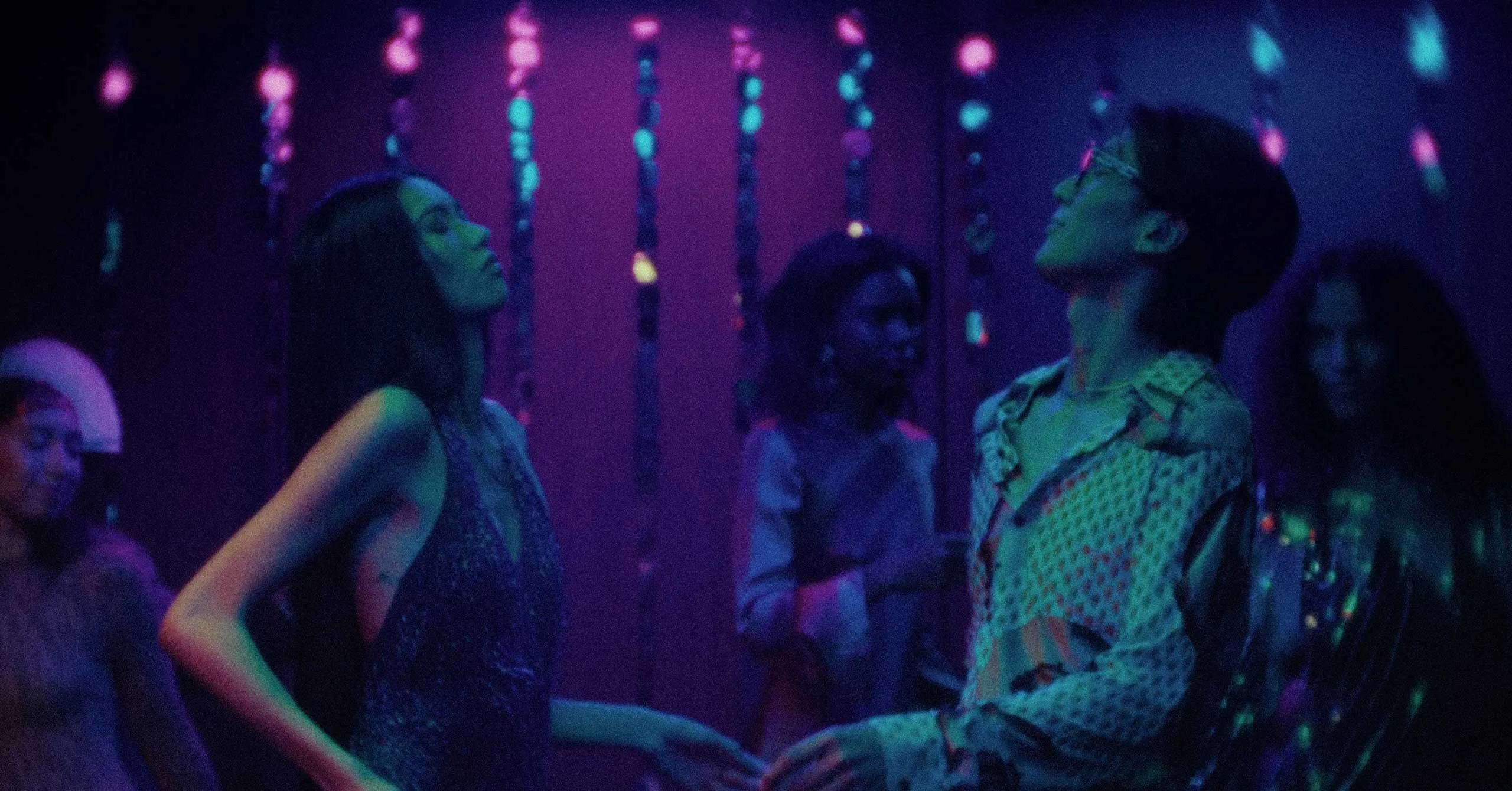 Dancers in a dark club under purple-blue neon lights, facing each other as they move to the music.