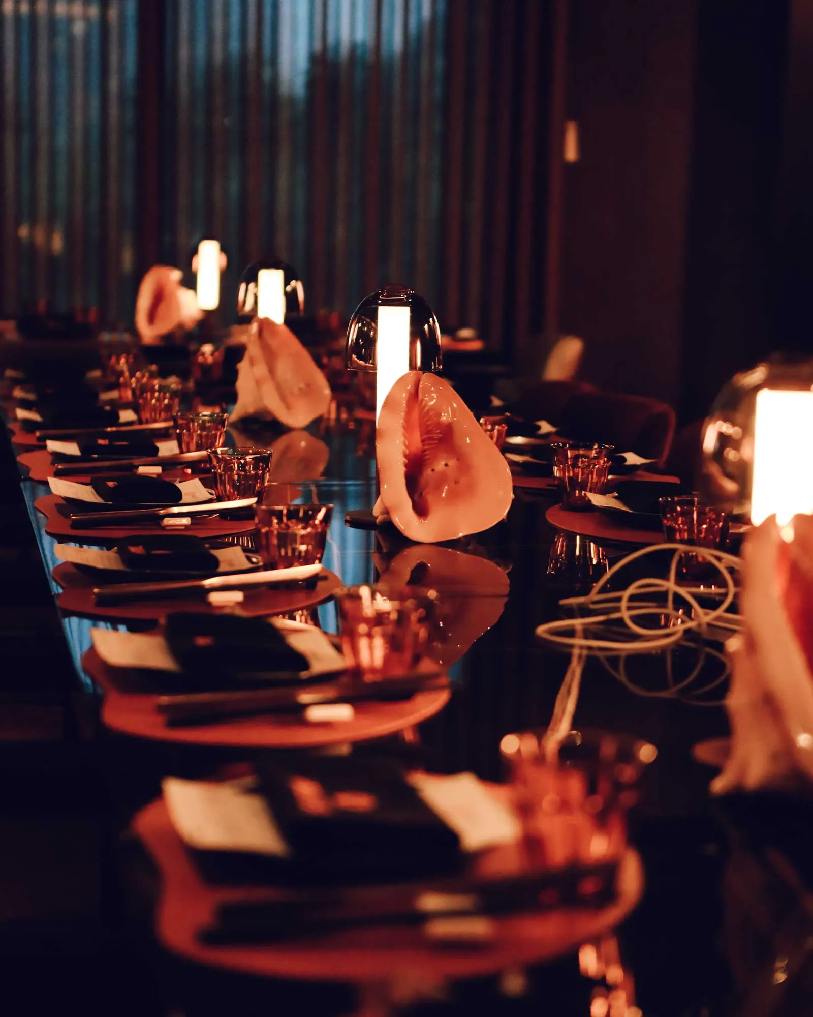 Dim, candlelit restaurant table with a large seashell centerpiece and glowing lamps along the table.