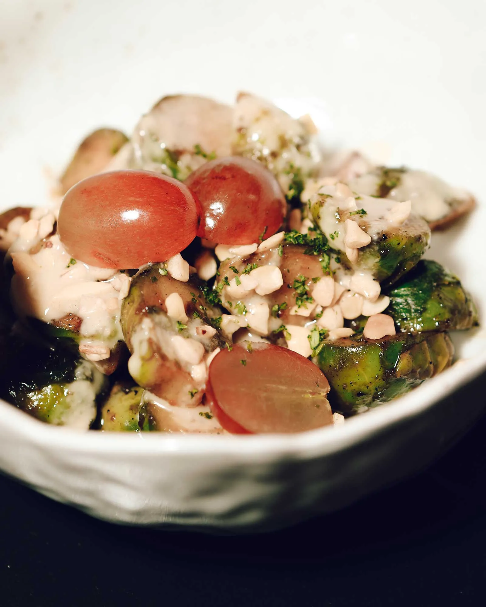 Close-up of a plated dish with cherry tomatoes, sliced zucchini, and a creamy herb sauce topped with chopped almonds and parsley fragments.