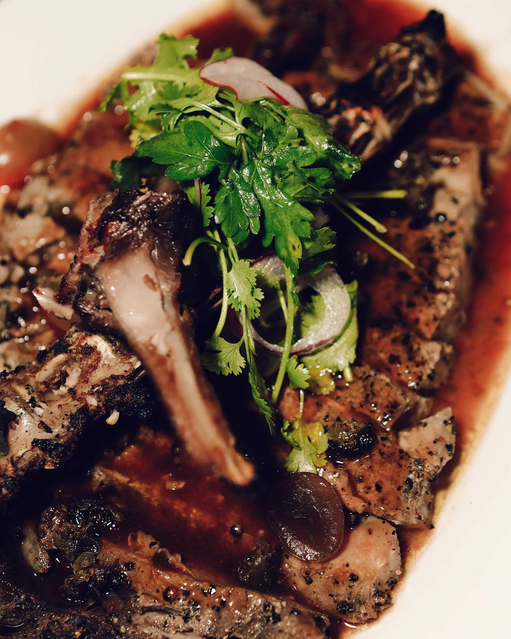 Grilled meat with a bright green parsley/cilantro garnish on top, glossy sauce visible on the surface.