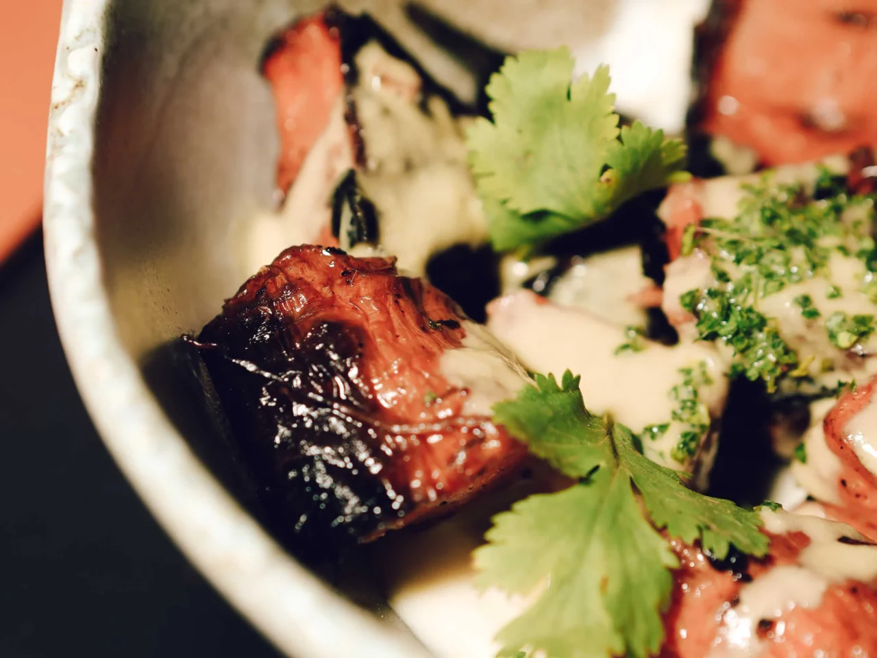 Grilled lamb chops on a plate with herbs, radish slices, and a glossy red sauce.