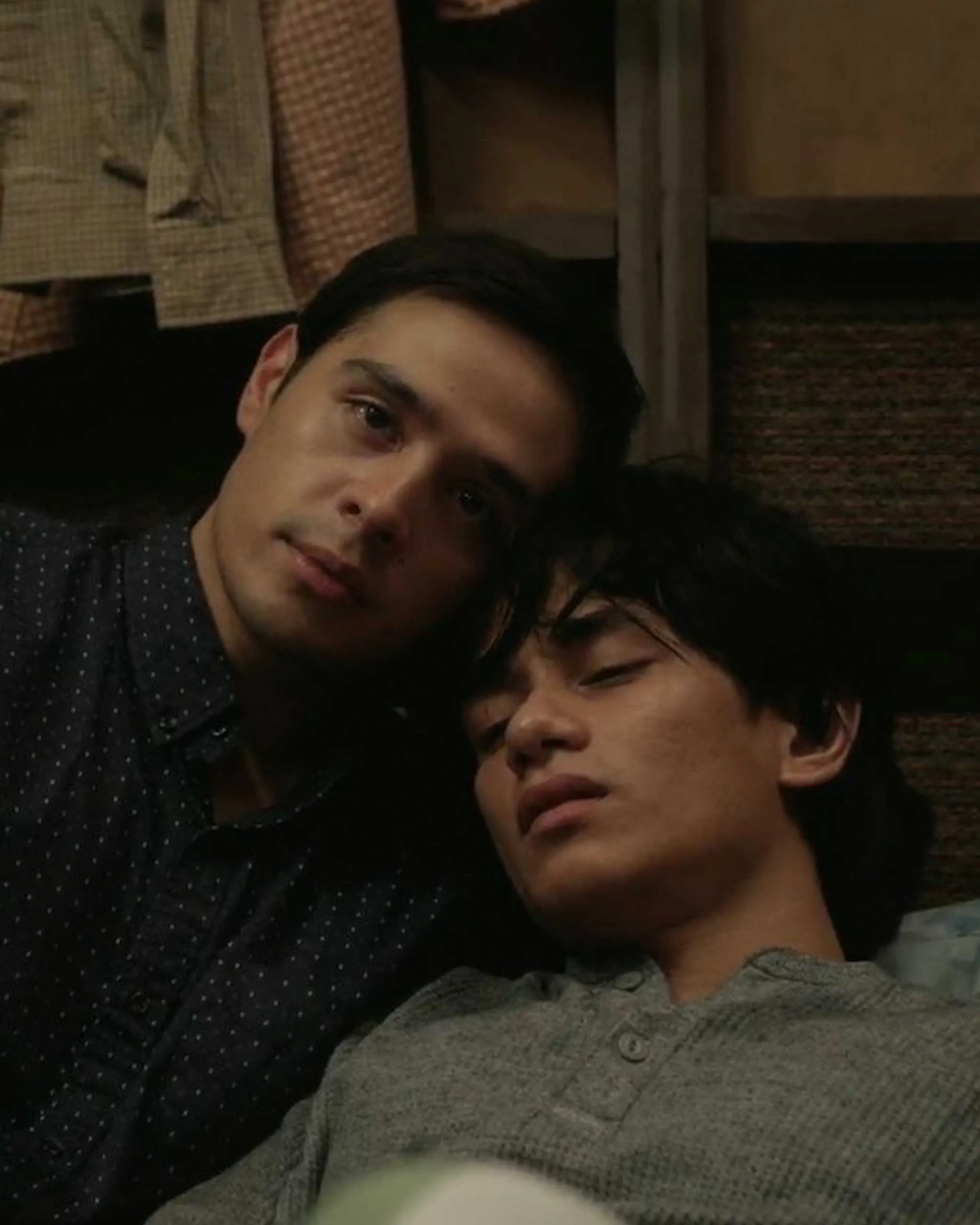 Two people lying close together, resting heads against one another in a dimly lit room for a casual selfie.