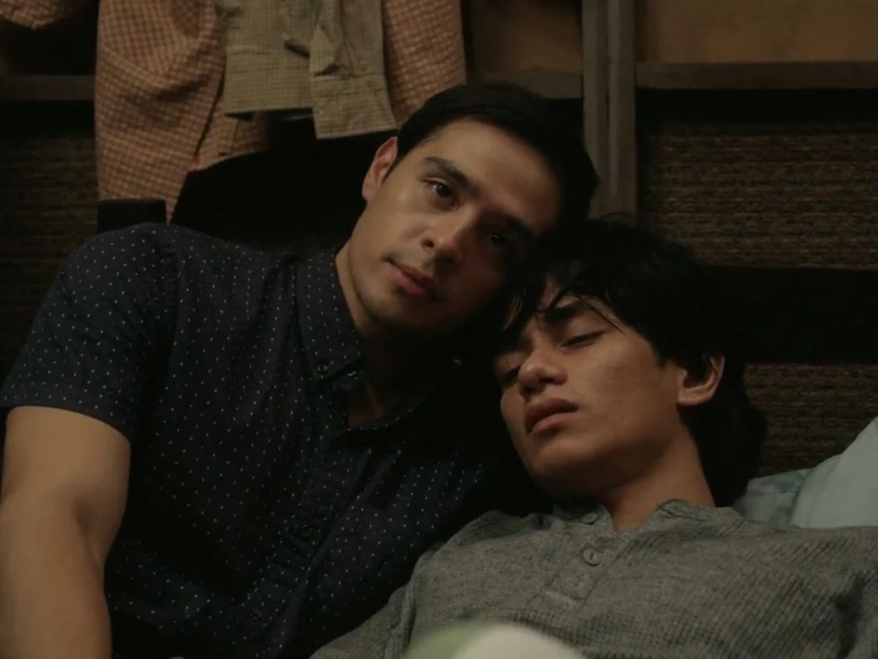Two young men snuggling on a couch, heads resting together and looking relaxed.