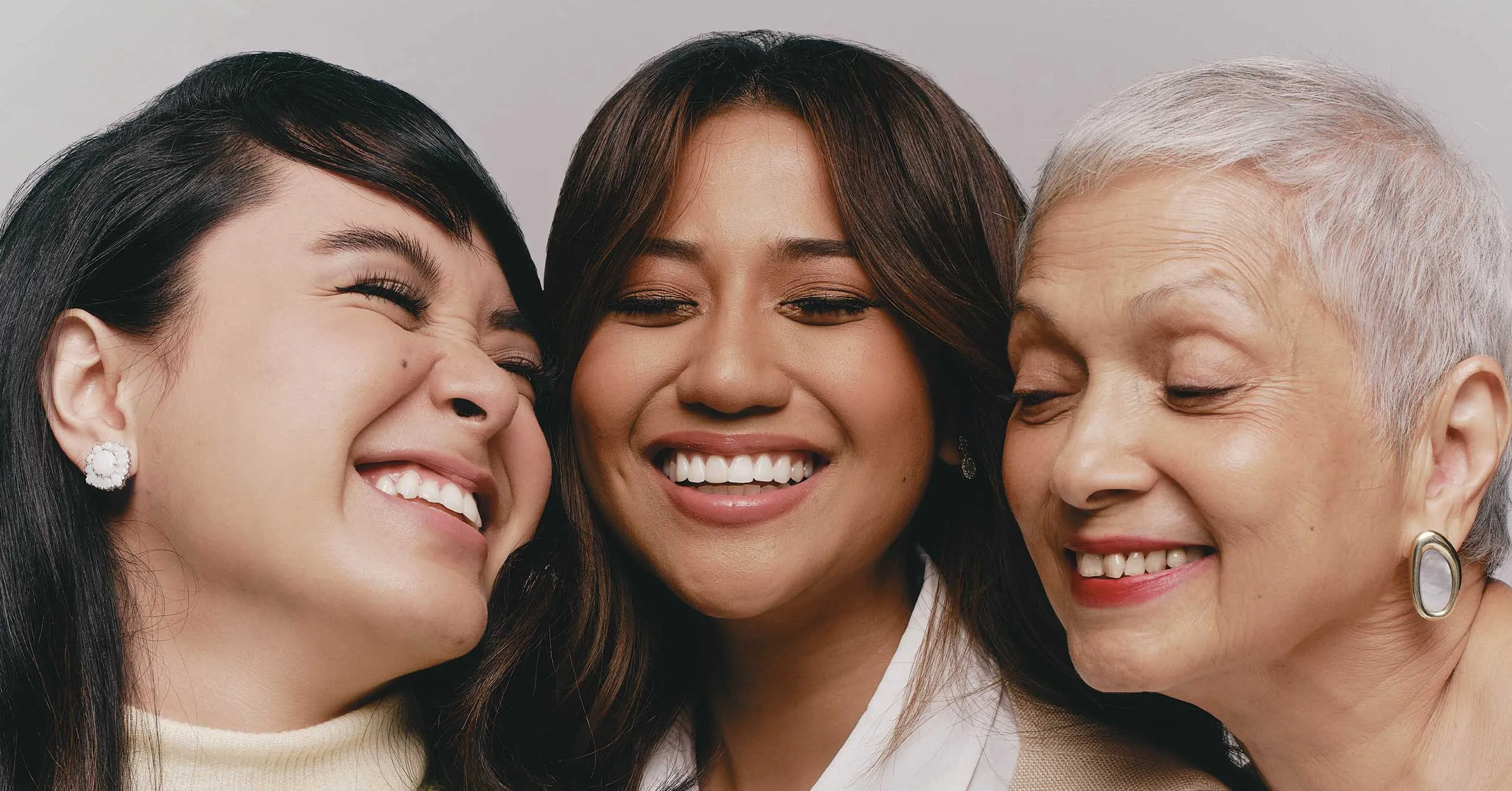 Three women of different ages smiling together in a close-up group portrait to show friendship and joy.