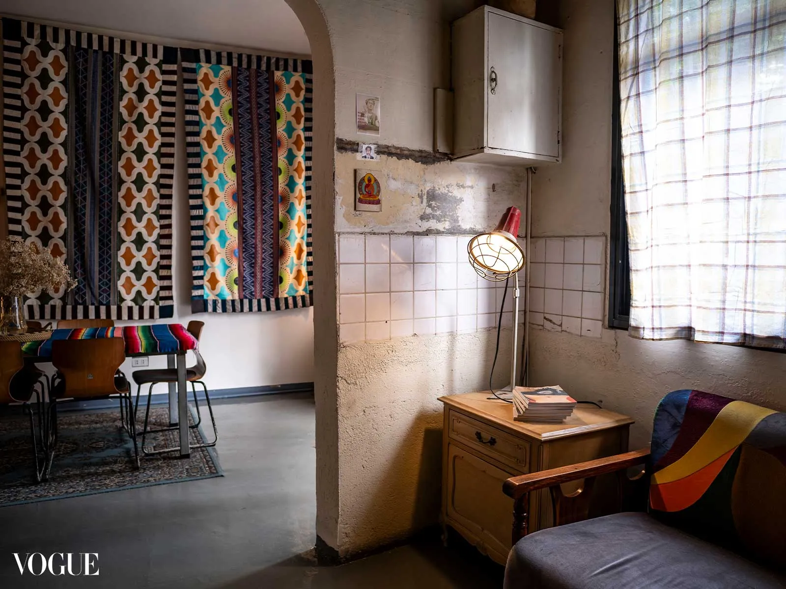 Colorful patterned textiles hang as wall art over a dining area with chairs and a rug.