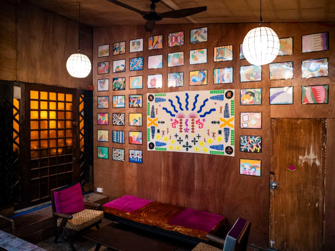 Cozy seating area with colorful patterned cushions along a dark wood-paneled wall and warm pendant light above.