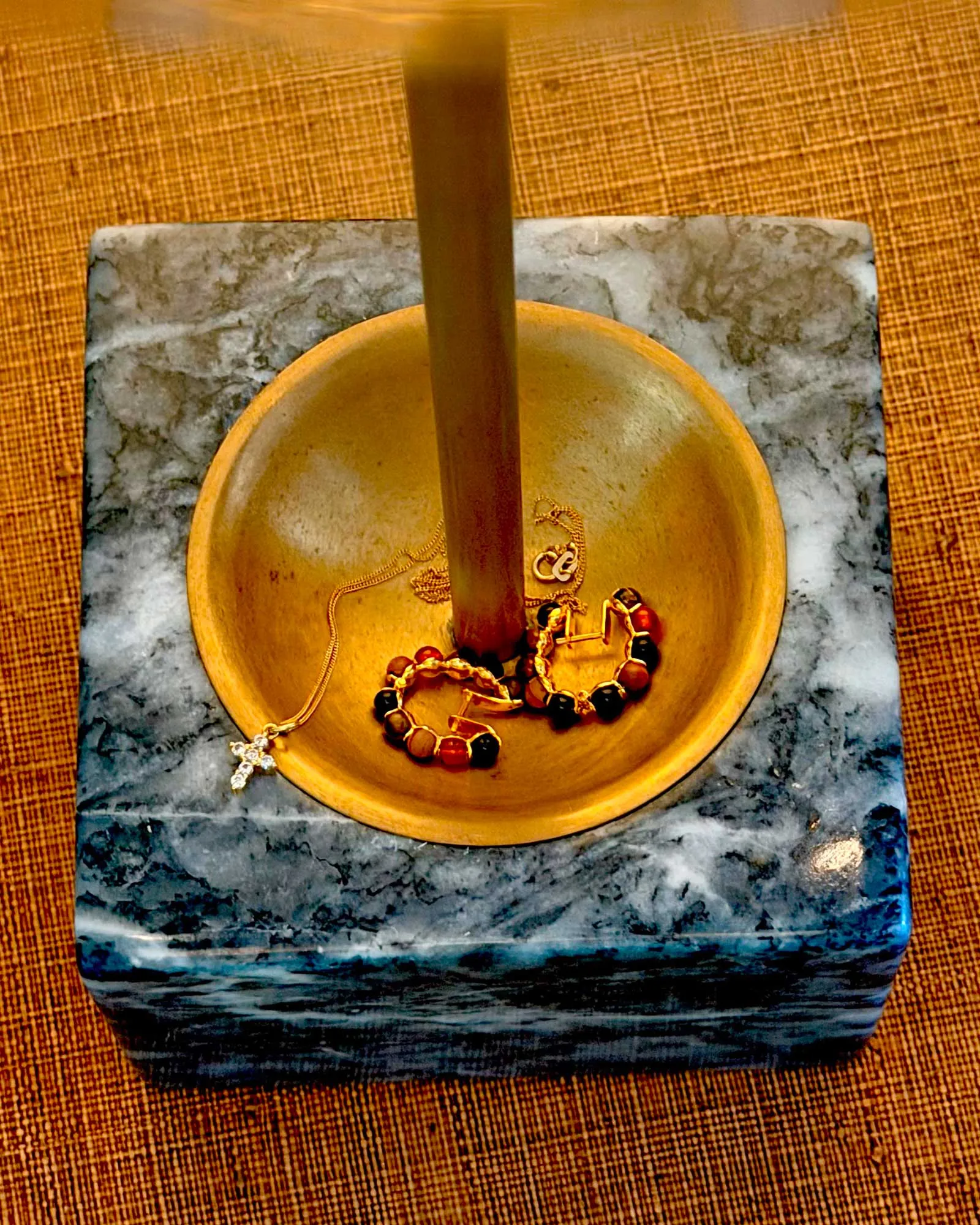 Gold bowl on a marble surface holding tangled jewelry, with a vertical wooden rod rising from the center.