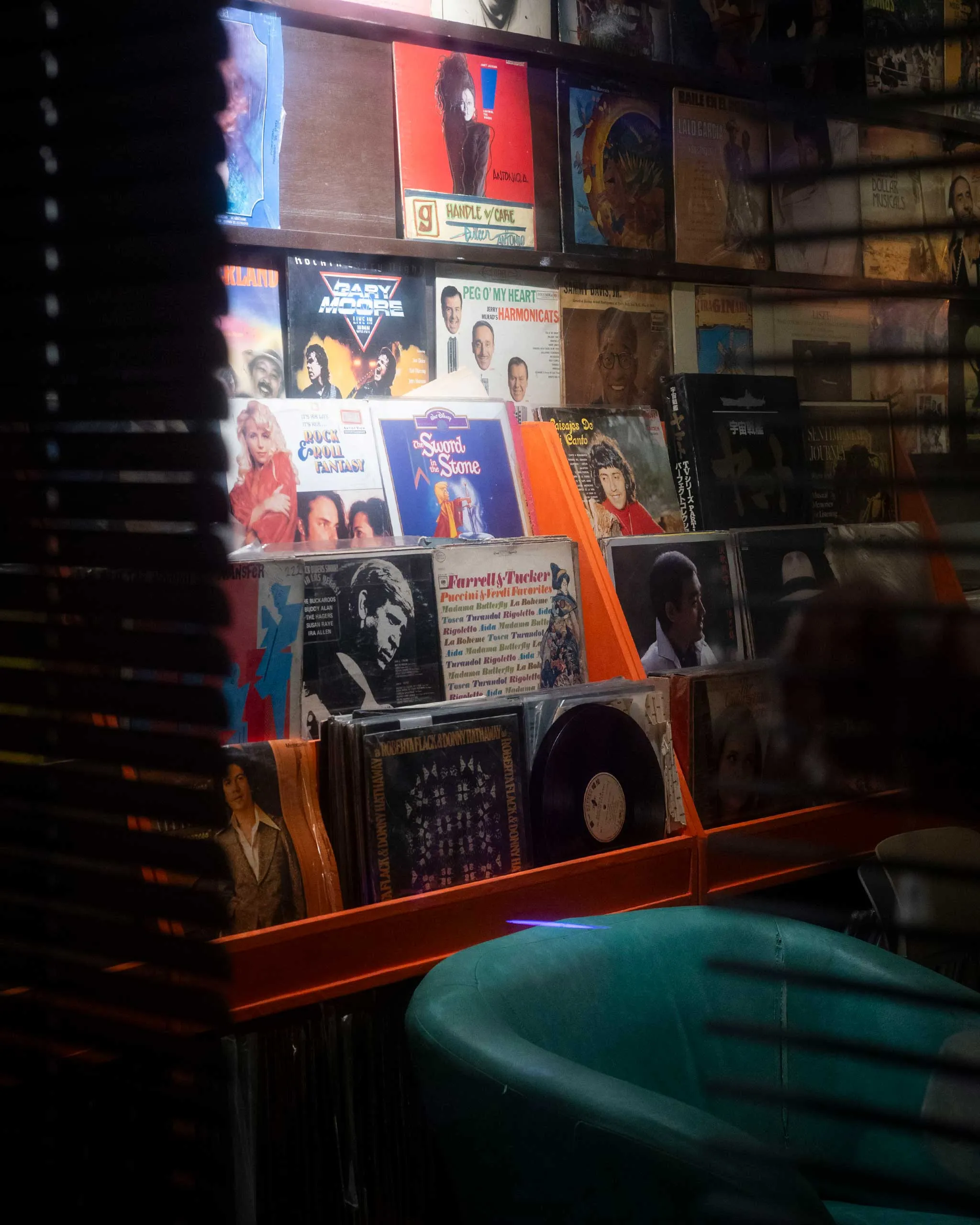 Wall of colorful vintage vinyl album covers displayed on wooden shelves in a dimly lit record shop.