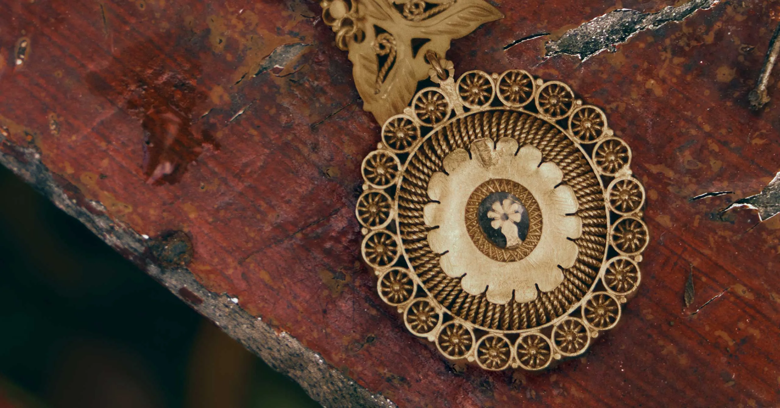 Ornate gold circular pendant with a floral center resting on a weathered rust-colored surface.