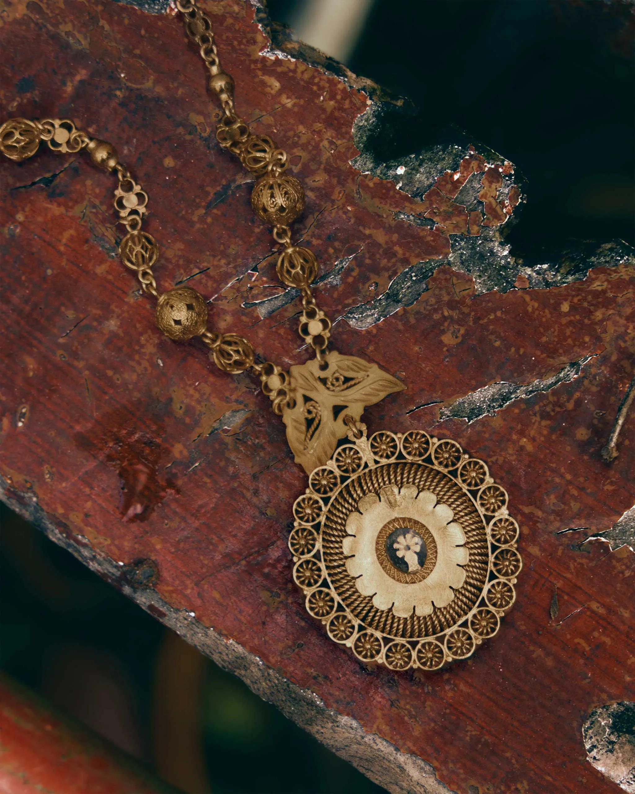 Gold ornamental necklace with a circular filigree pendant resting on a rusted, textured surface.