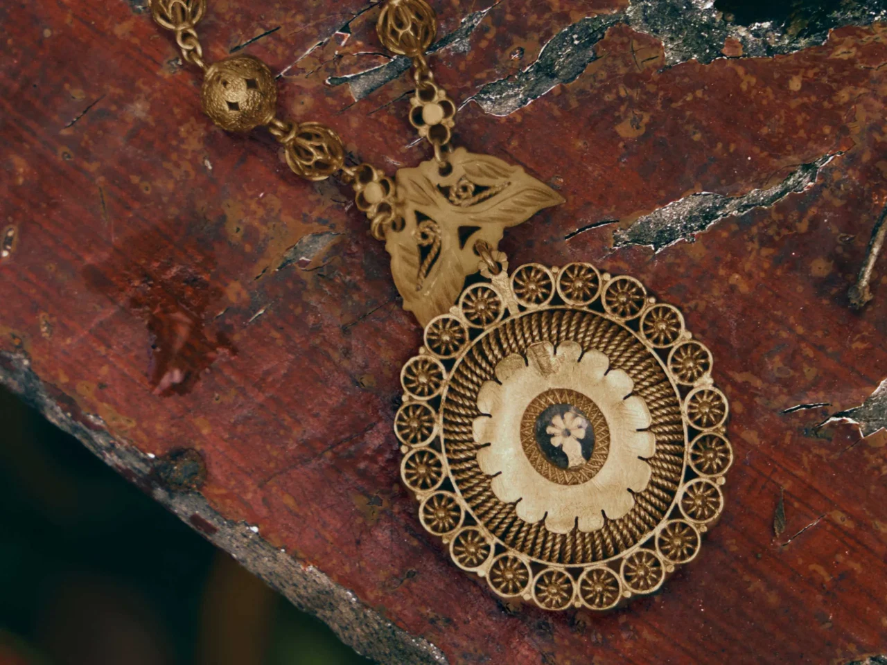 Ornate gold circular pendant with a floral center resting on a weathered rust-colored surface.