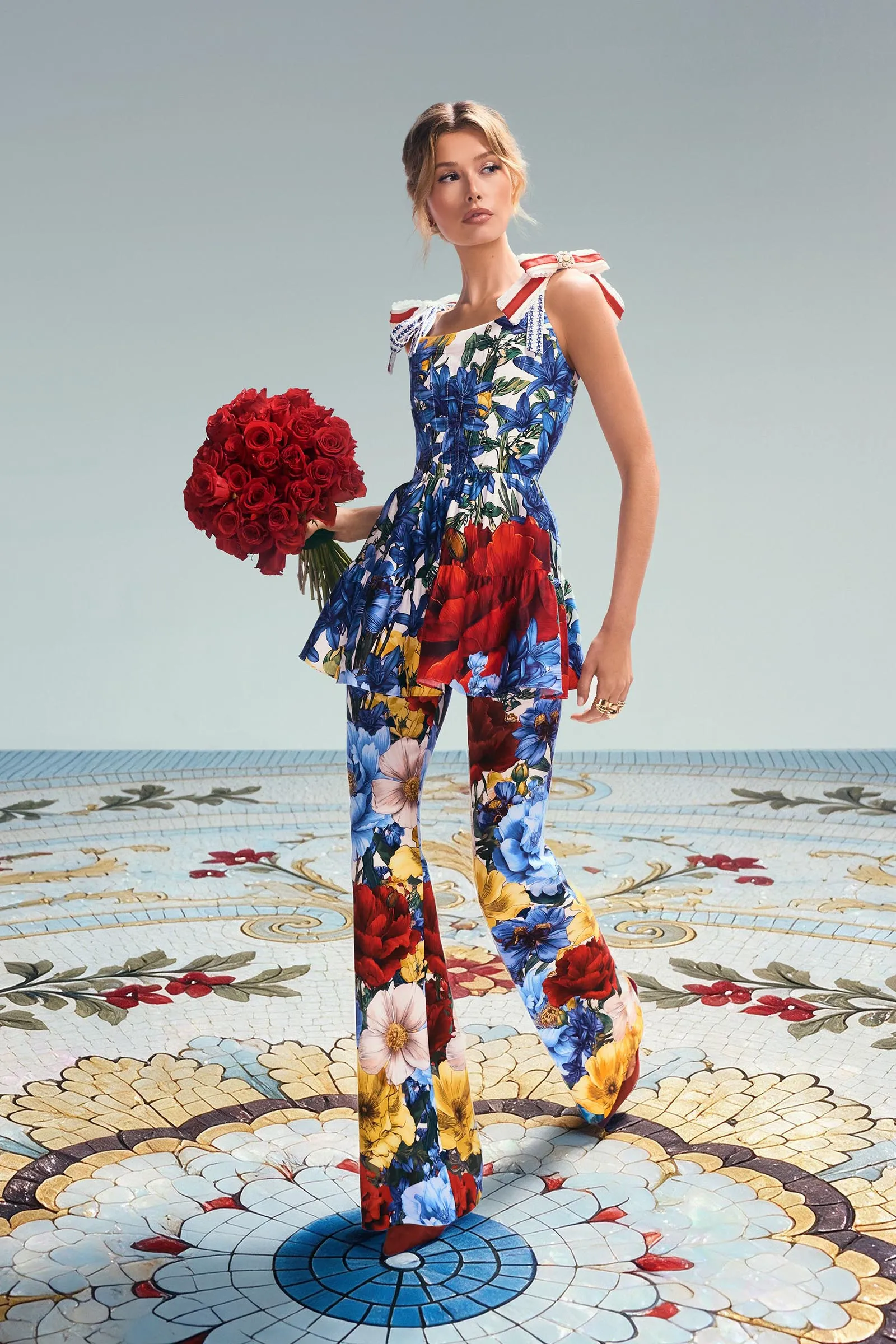 Woman in a colorful floral jumpsuit holding a bouquet of red roses on a decorative tiled floor.