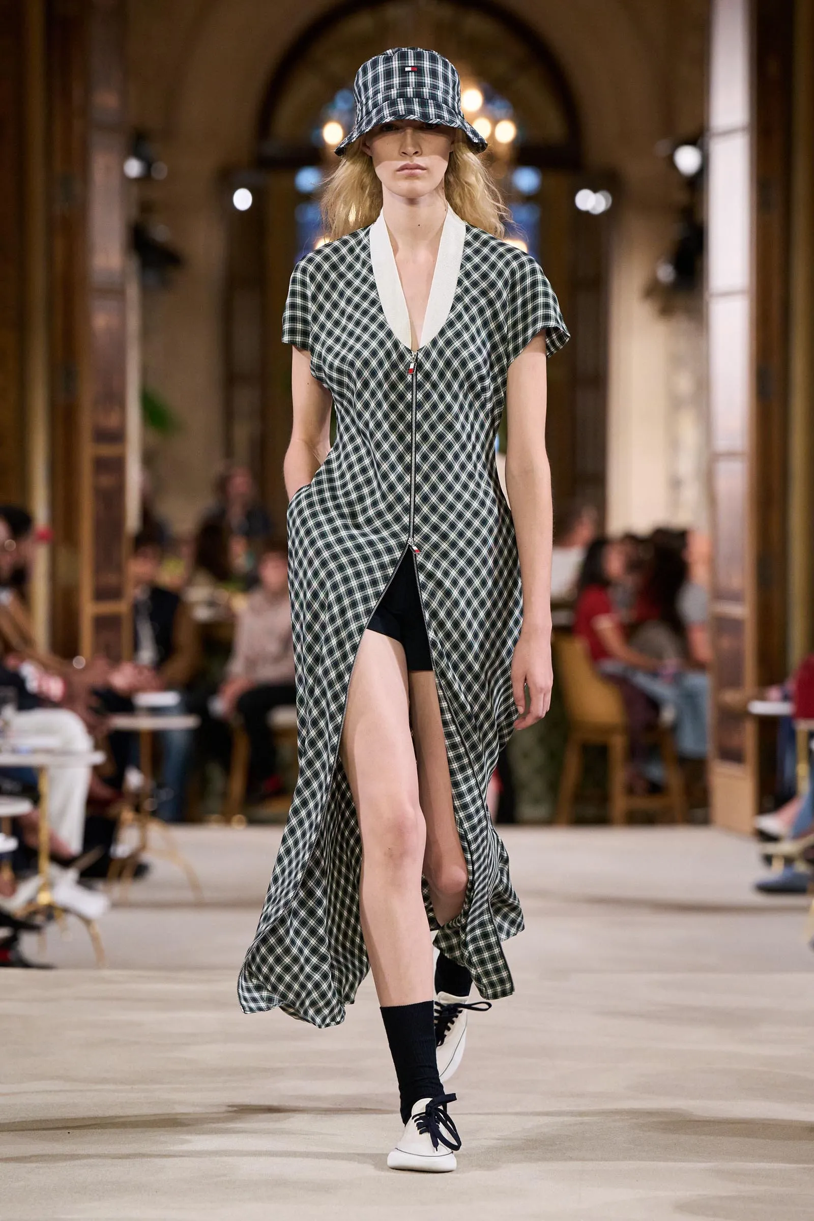 Model walks a fashion runway wearing a black-and-white checkered outfit with a matching bucket hat, white trim, and sneakers.