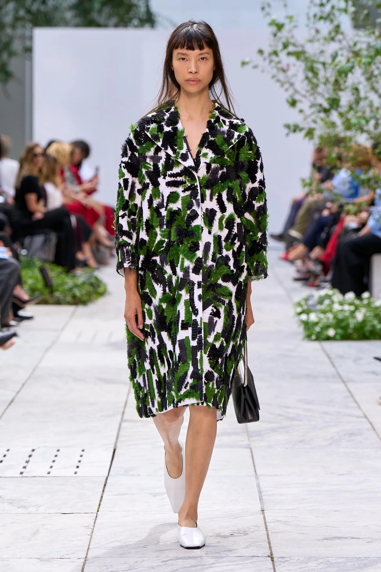 Runway model wearing a bold black, green, and white textured coat with a brushstroke pattern.