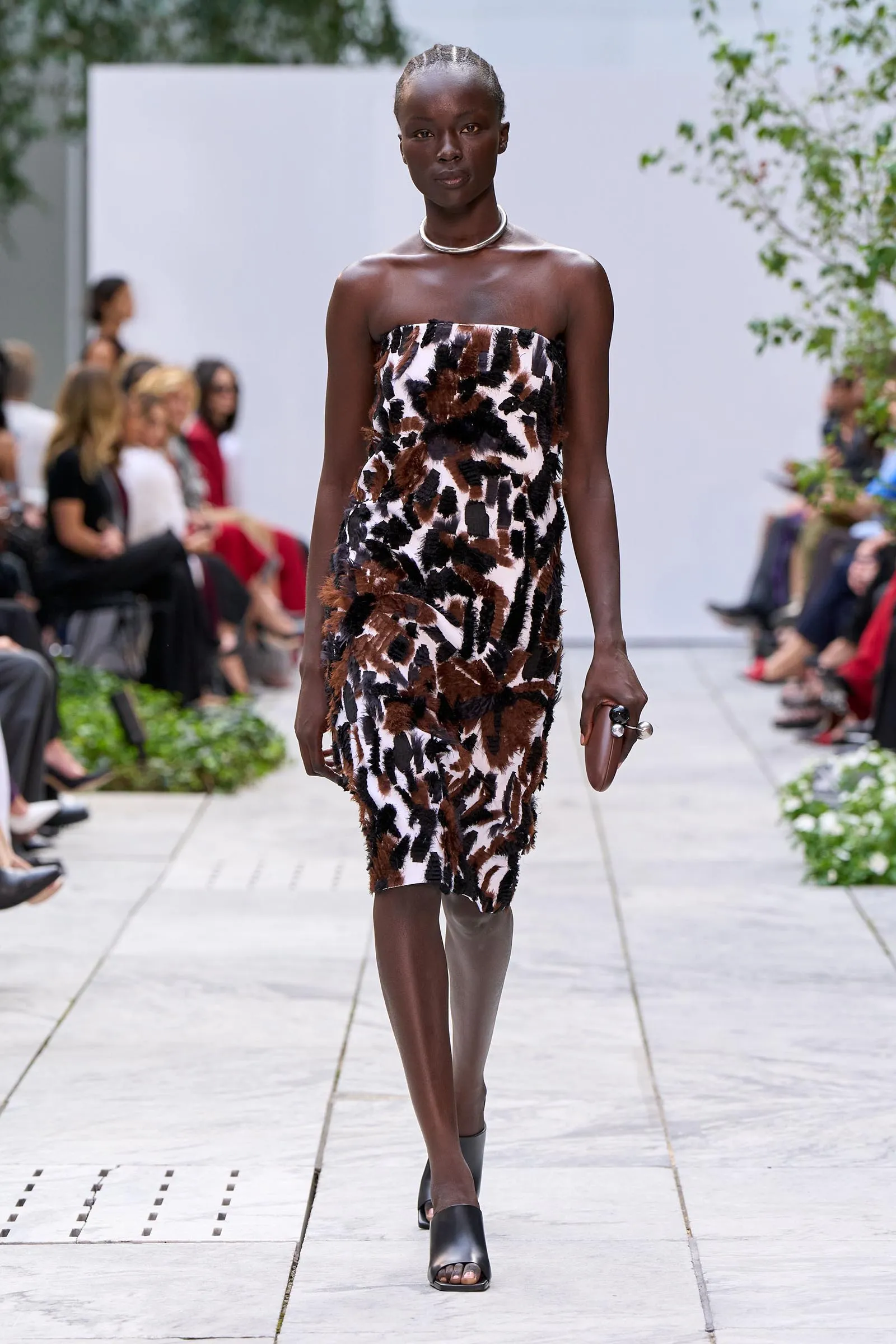 Model walking the runway in a strapless animal-print dress with a silver choker and black open-toe sandals, holding a small clutch.