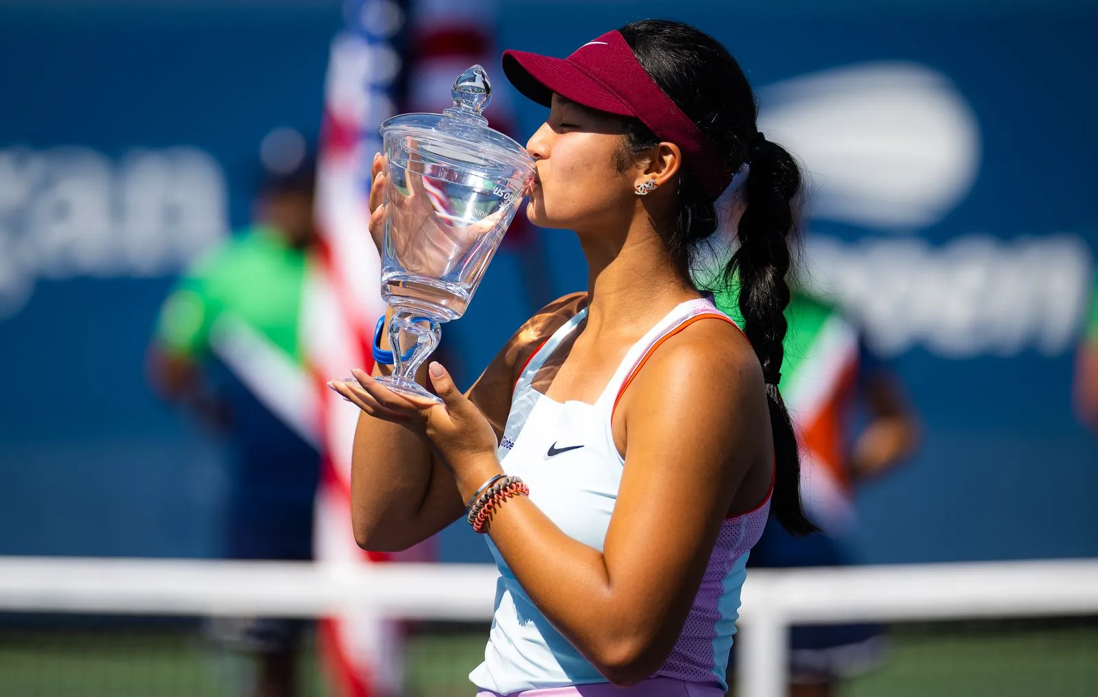 Tennis player celebrates victory by kissing a crystal trophy on a sunny court