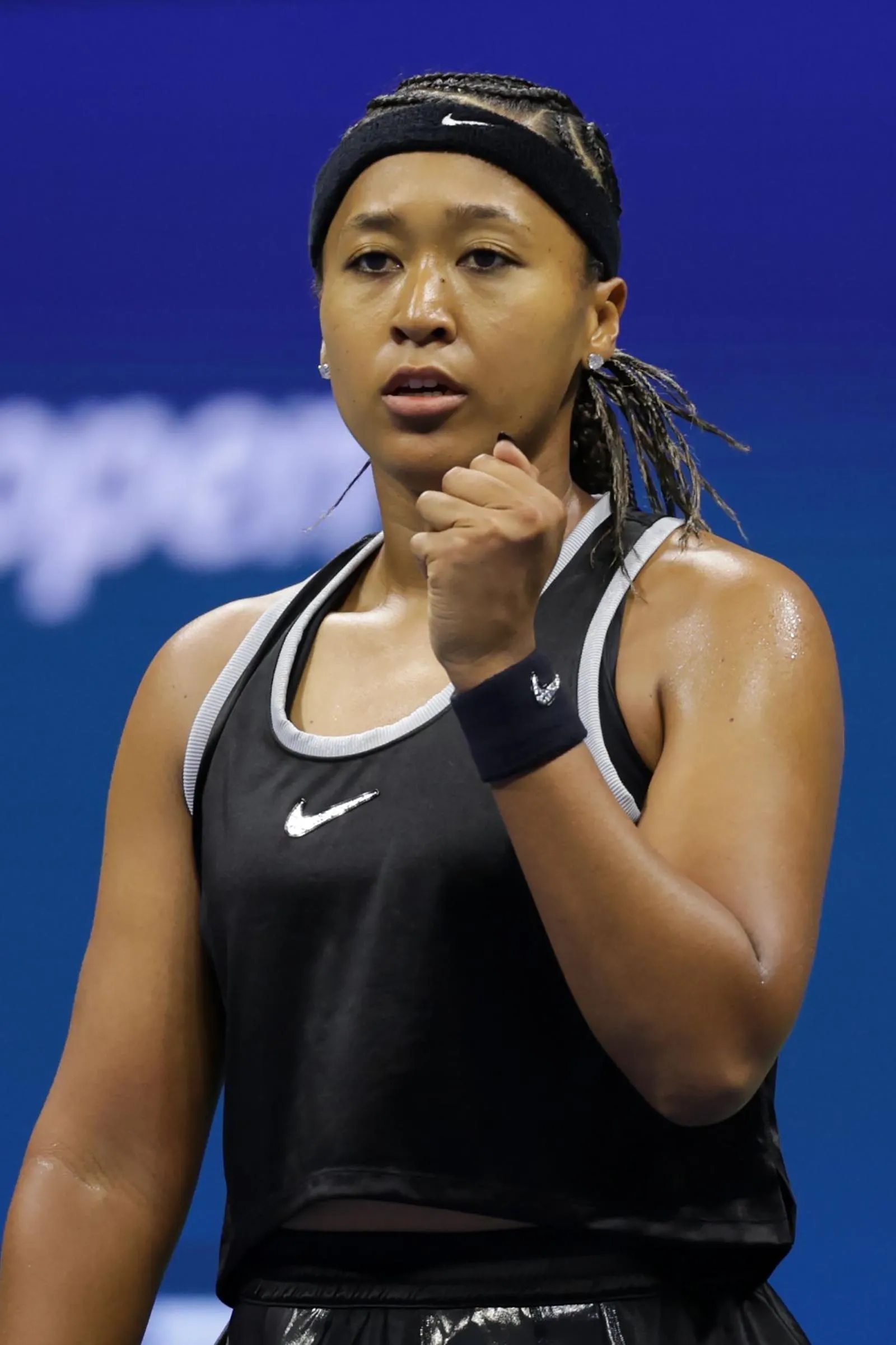 Female tennis player in a black Nike tank top and headband fist-pumping, appearing focused against a blue background.