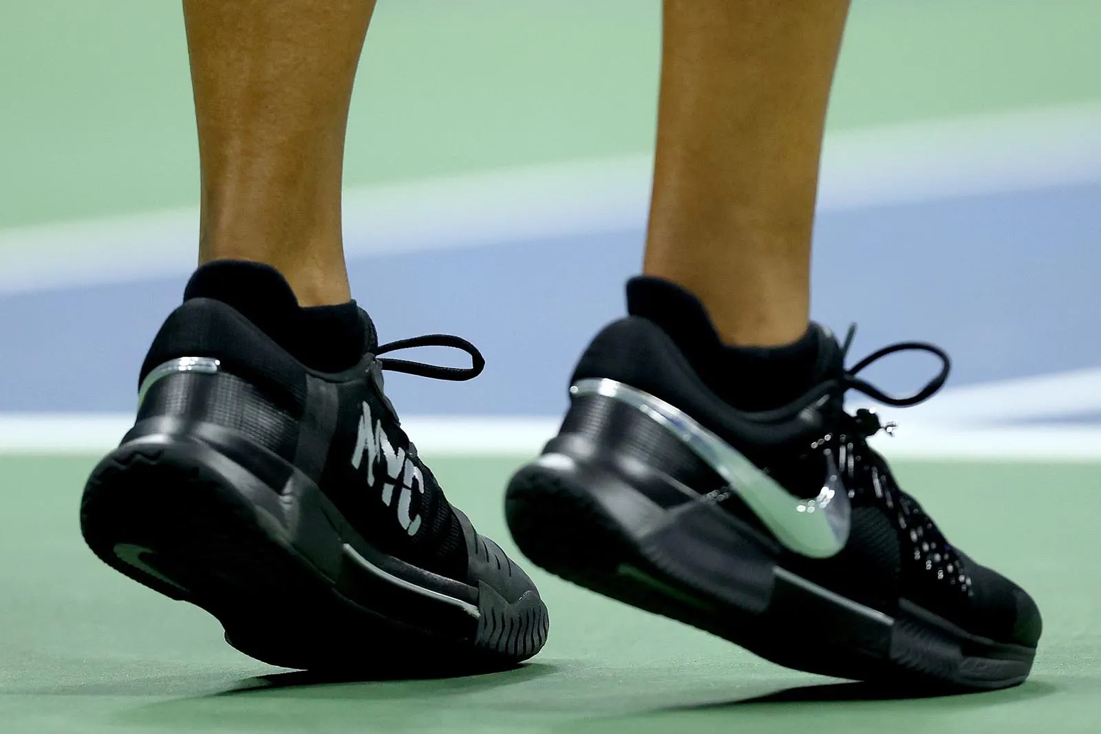 Black athletic sneakers with a white Nike swoosh, mid-step on a green court surface.