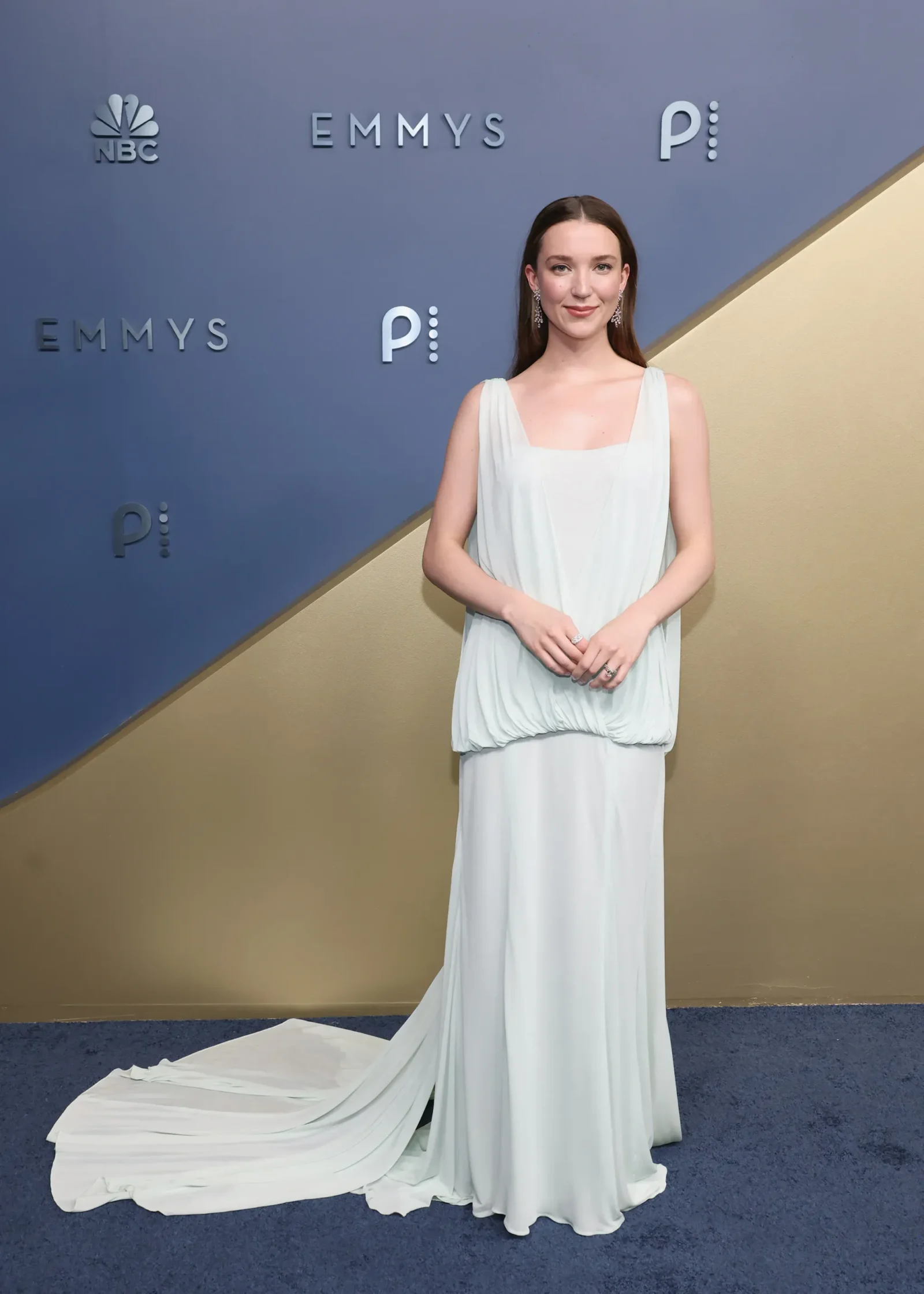 Woman in a light blue gown poses on a blue and gold backdrop with Emmy logos behind her and dotted décor accents.