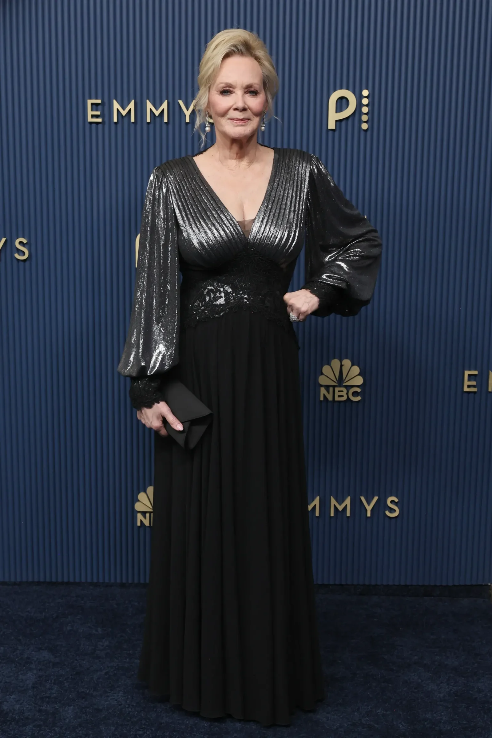 Woman in a long black gown with a metallic-silver pleated bodice posing on the Emmy Awards blue backdrop.