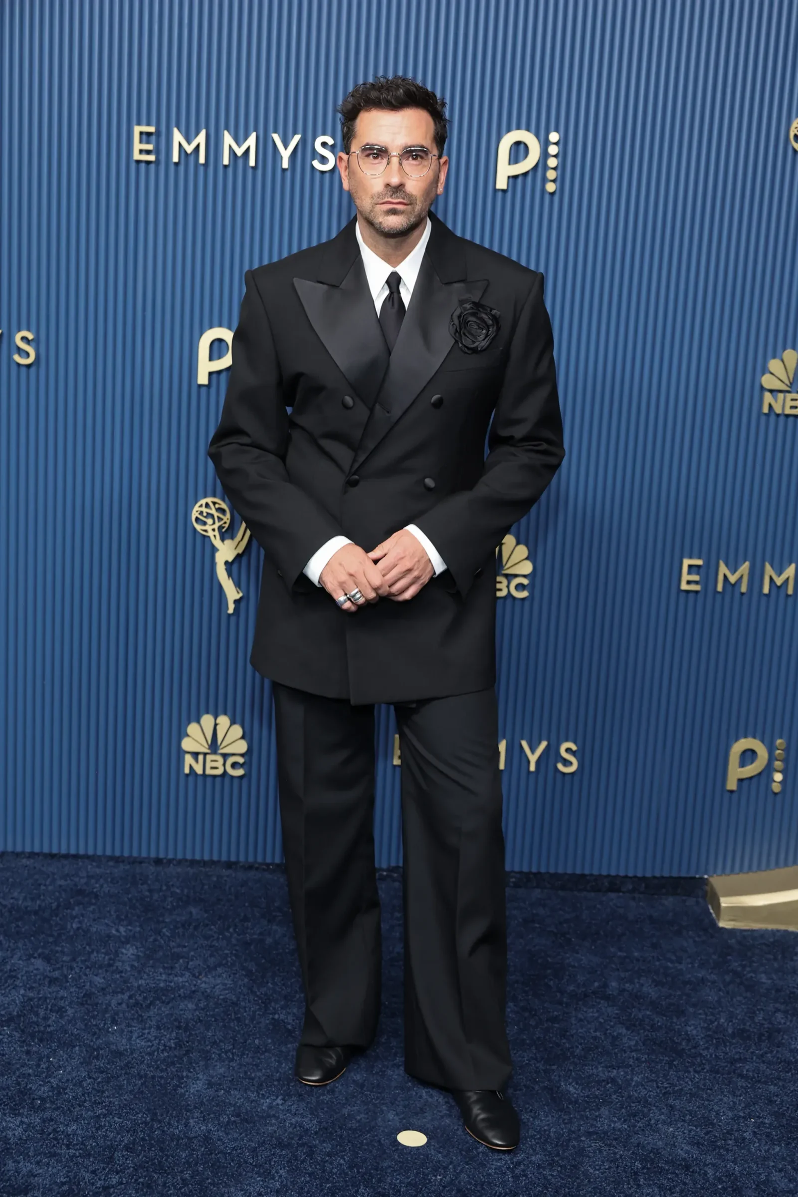 Man in a double-breasted black suit with glasses posing on a blue Emmy backdrop