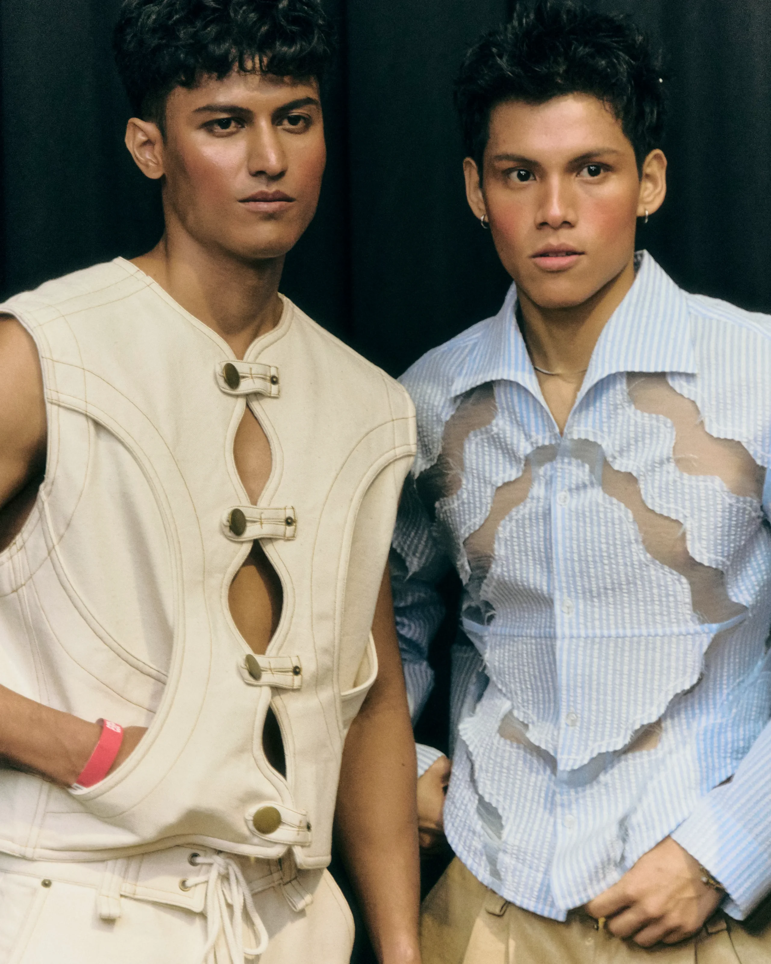 Two models posing side by side: left in a cream sleeveless vest, right in a distressed blue striped shirt.