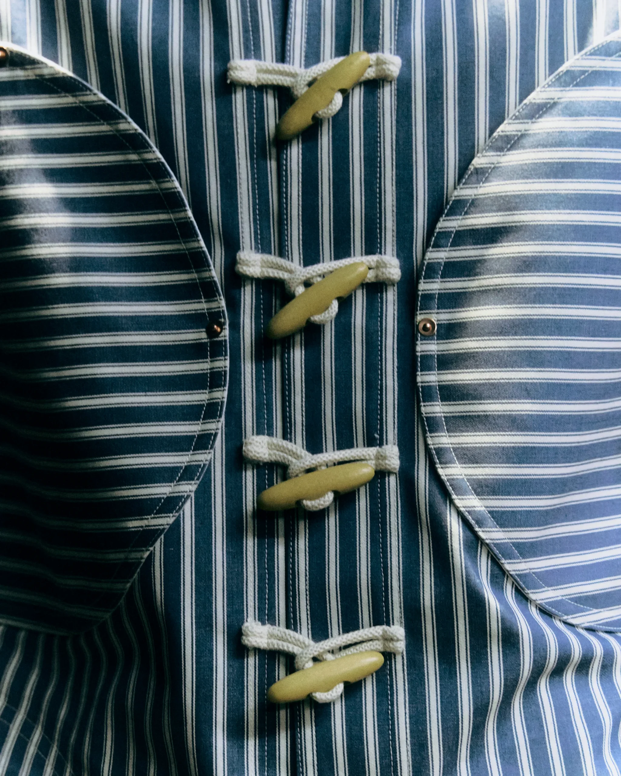 Close-up of a blue striped fabric with white rope loops and tan frog closures down the front.