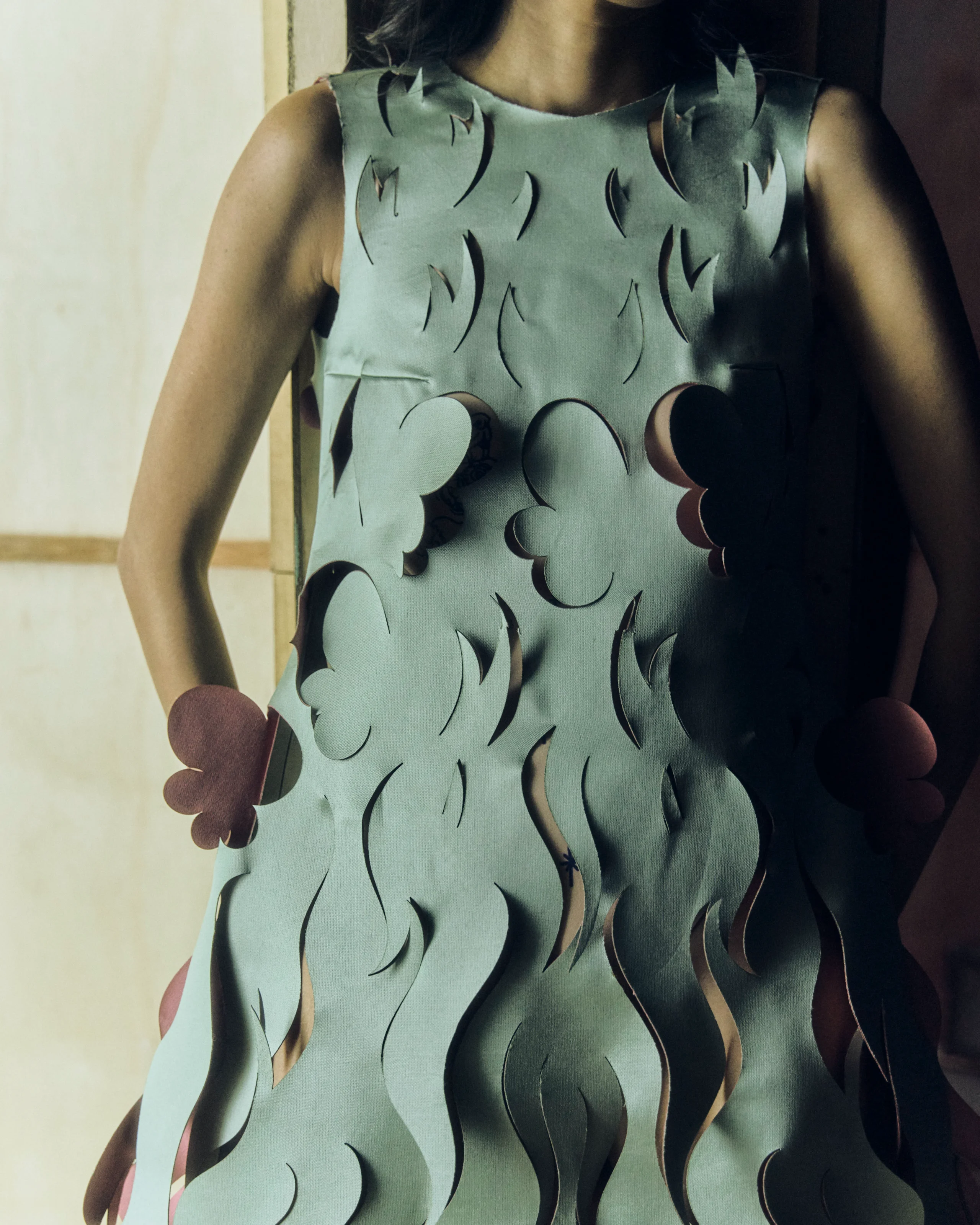 Close-up of a pale blue sleeveless dress with black flame-like cutouts along the fabric, shown from shoulders to torso.