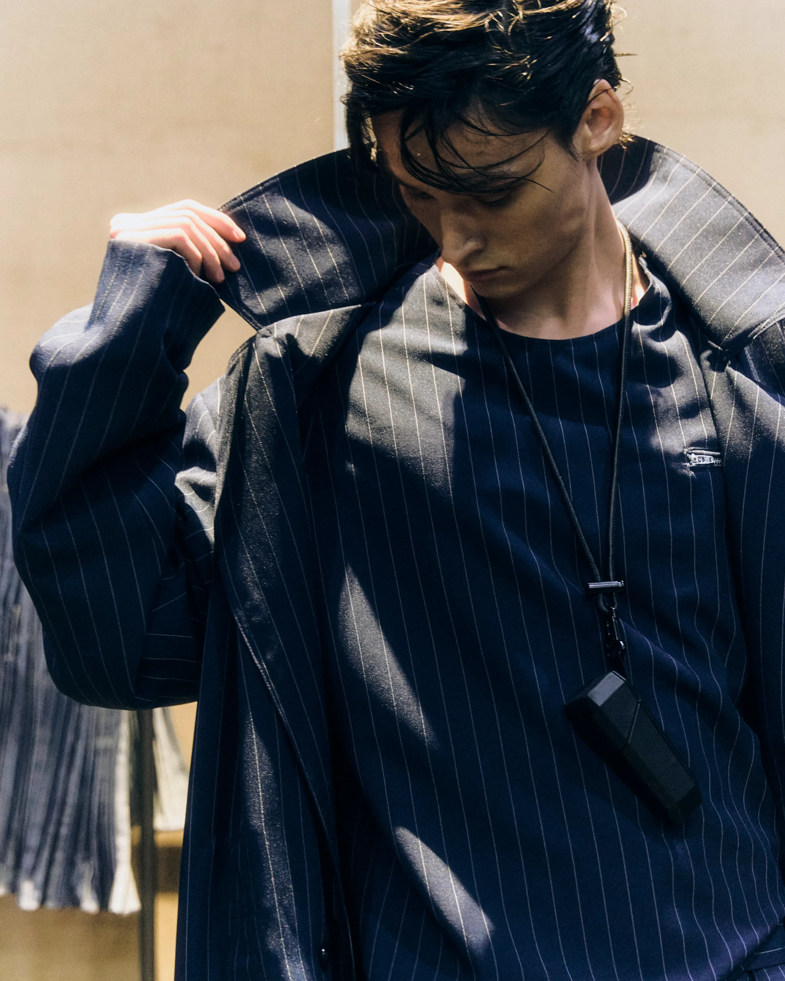 Man in a dark pinstripe suit looking down while adjusting his jacket at chest height.