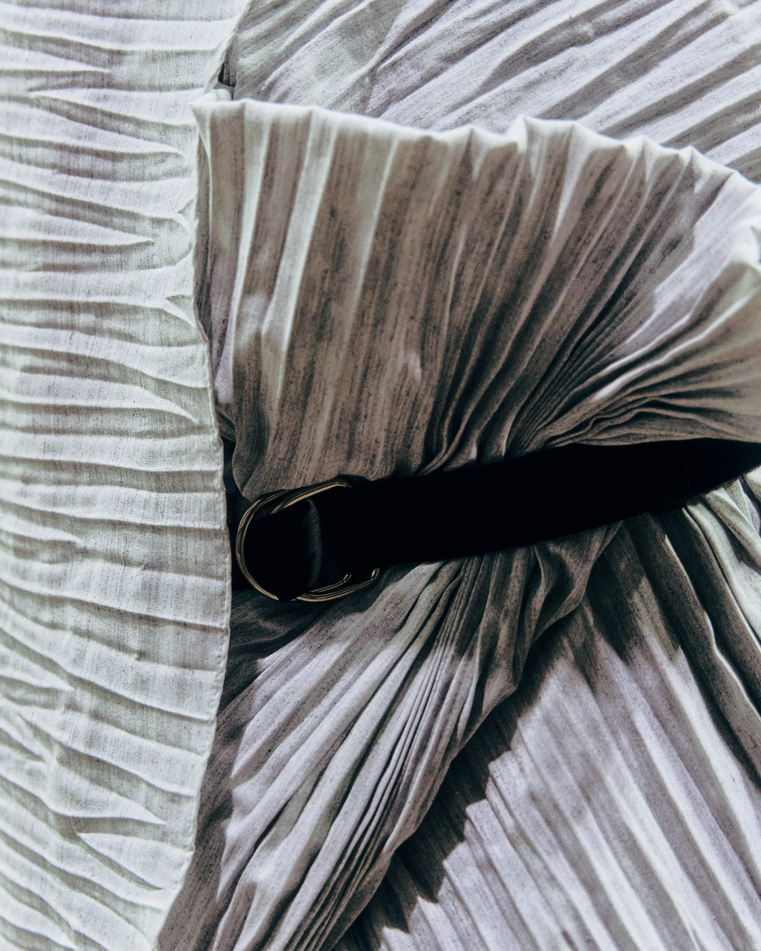 Close-up of light gray pleated fabric with deep folds and shadows.