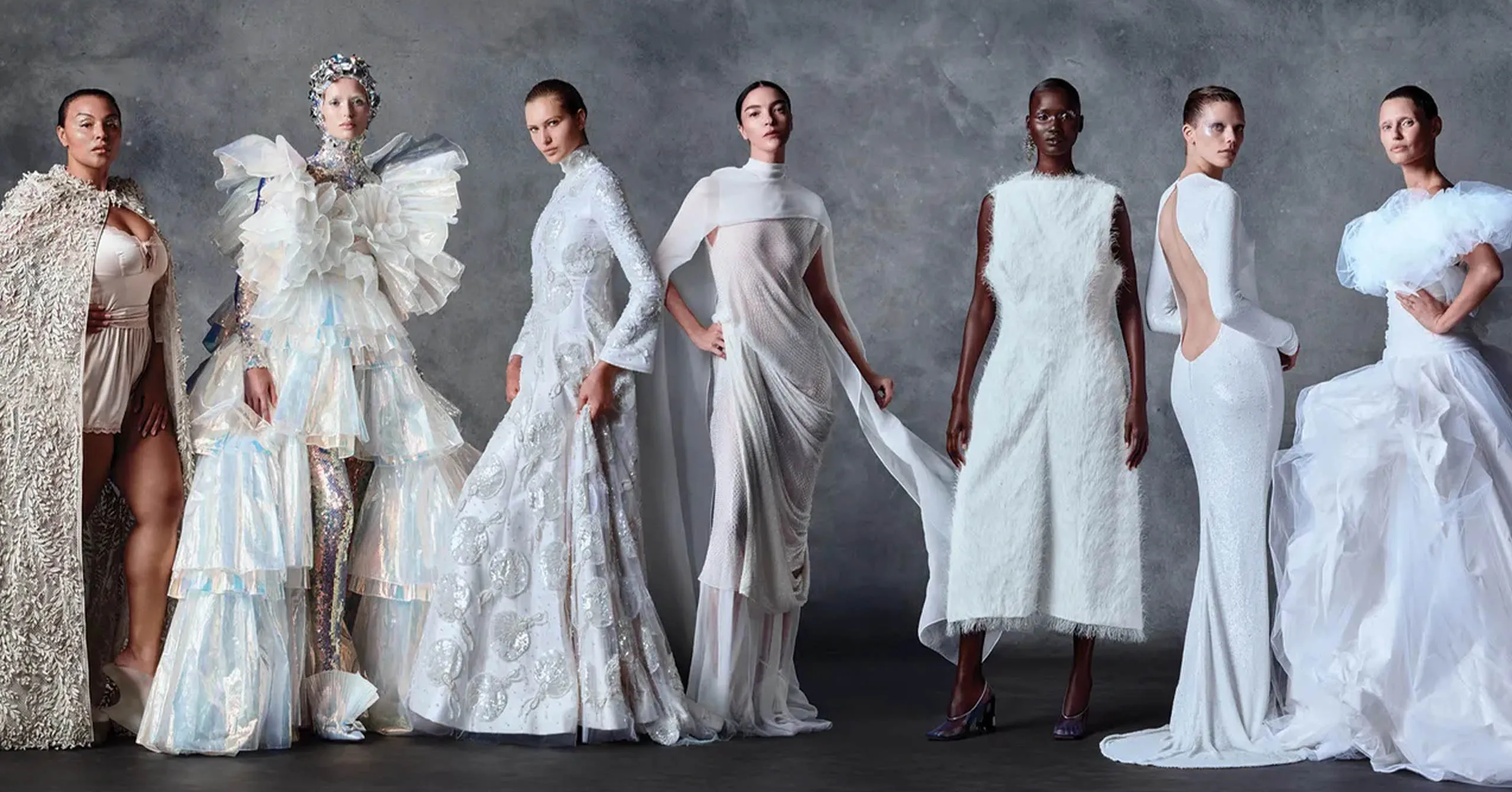 Eight models pose in a lineup wearing dramatic white couture gowns in a studio setting