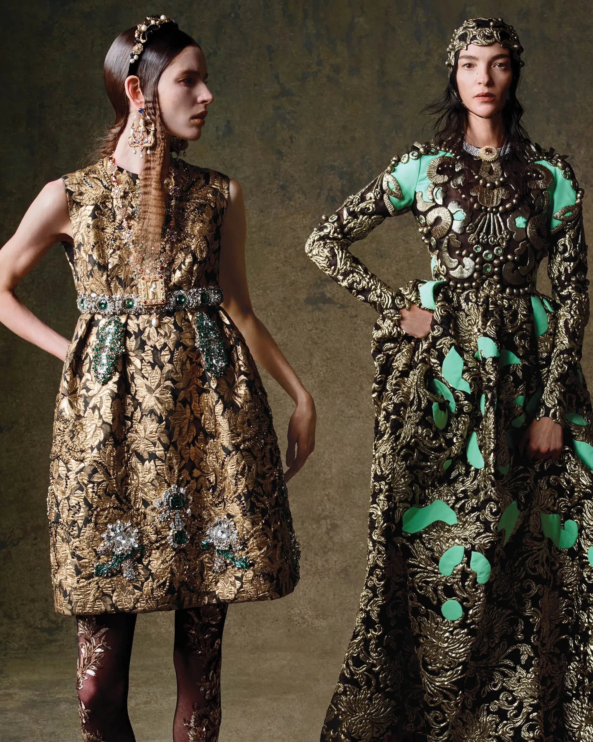 Two models wear opulent gold brocade gowns with heavy embroidery and jeweled accessories, posing against a textured backdrop.