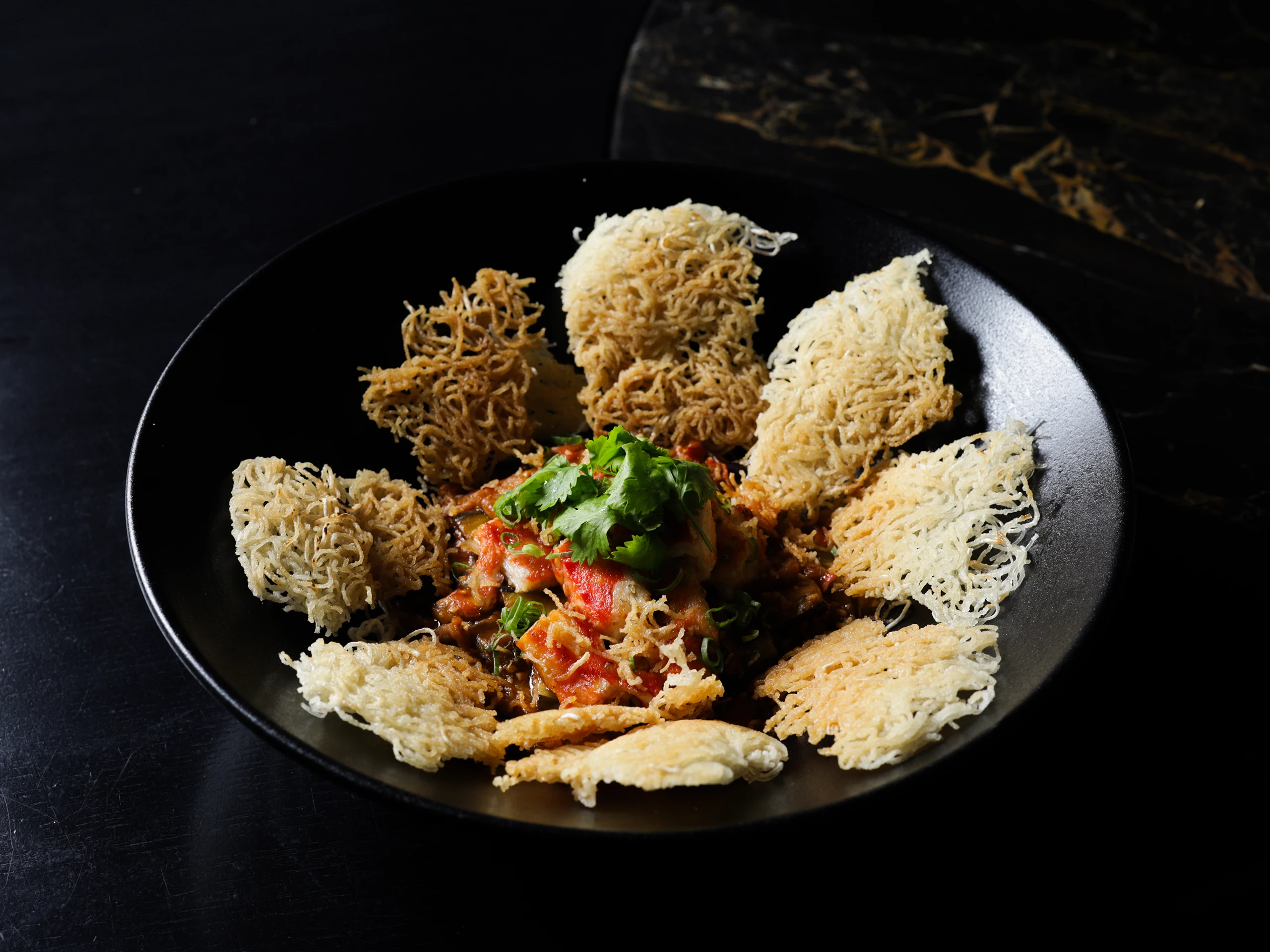 Crispy, lattice-fried nest shapes arranged on a dark plate over a tomato-herb sauce garnish.