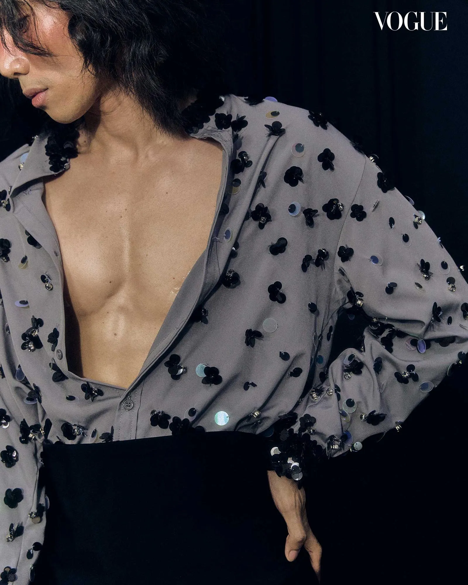Model wearing a gray sequined blouse with black floral embellishments, partial face visible, Vogue logo in the corner.