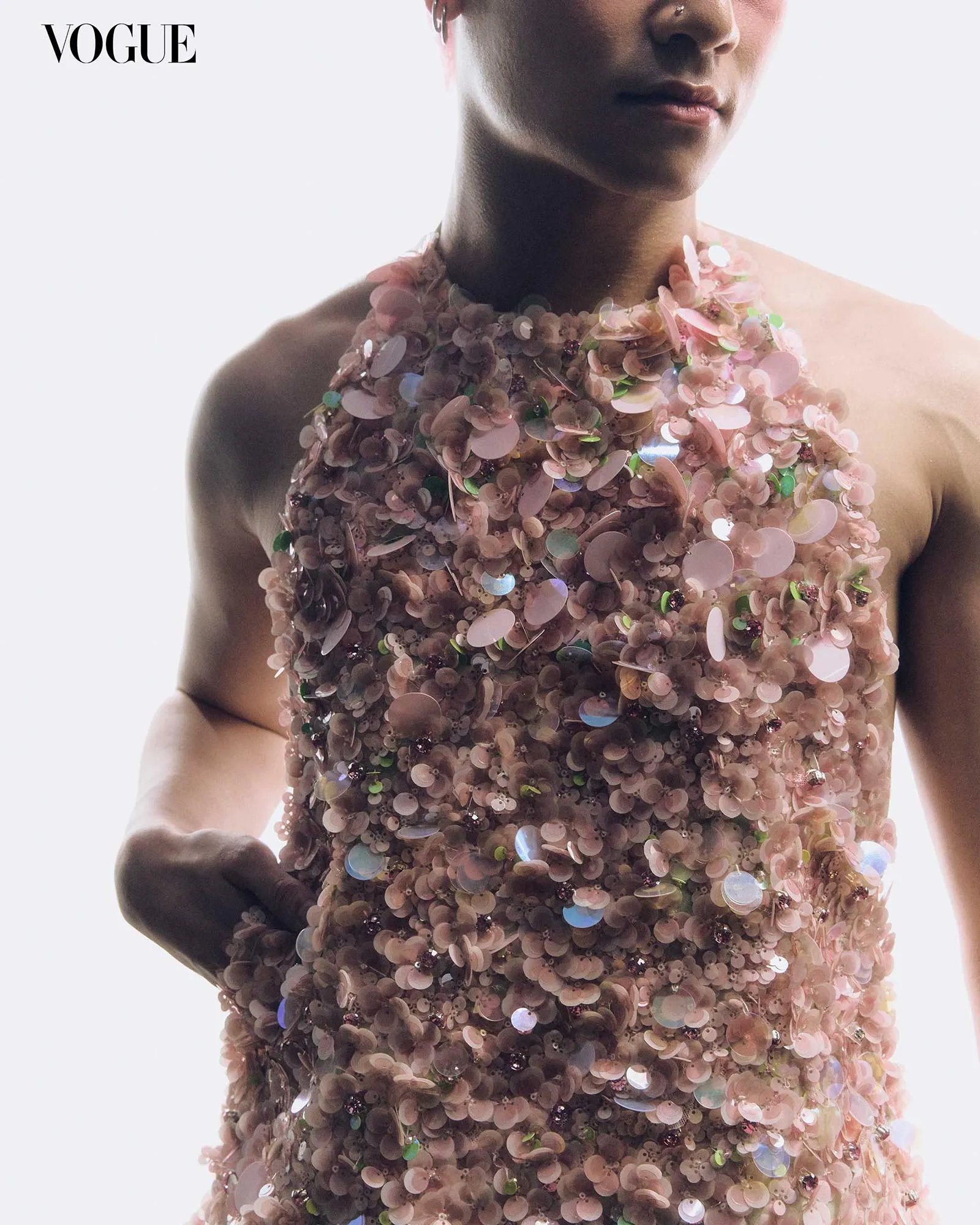 Vogue logo in the top left with a close-up of a person wearing a pink sequin-covered dress that covers the chest and shoulders.