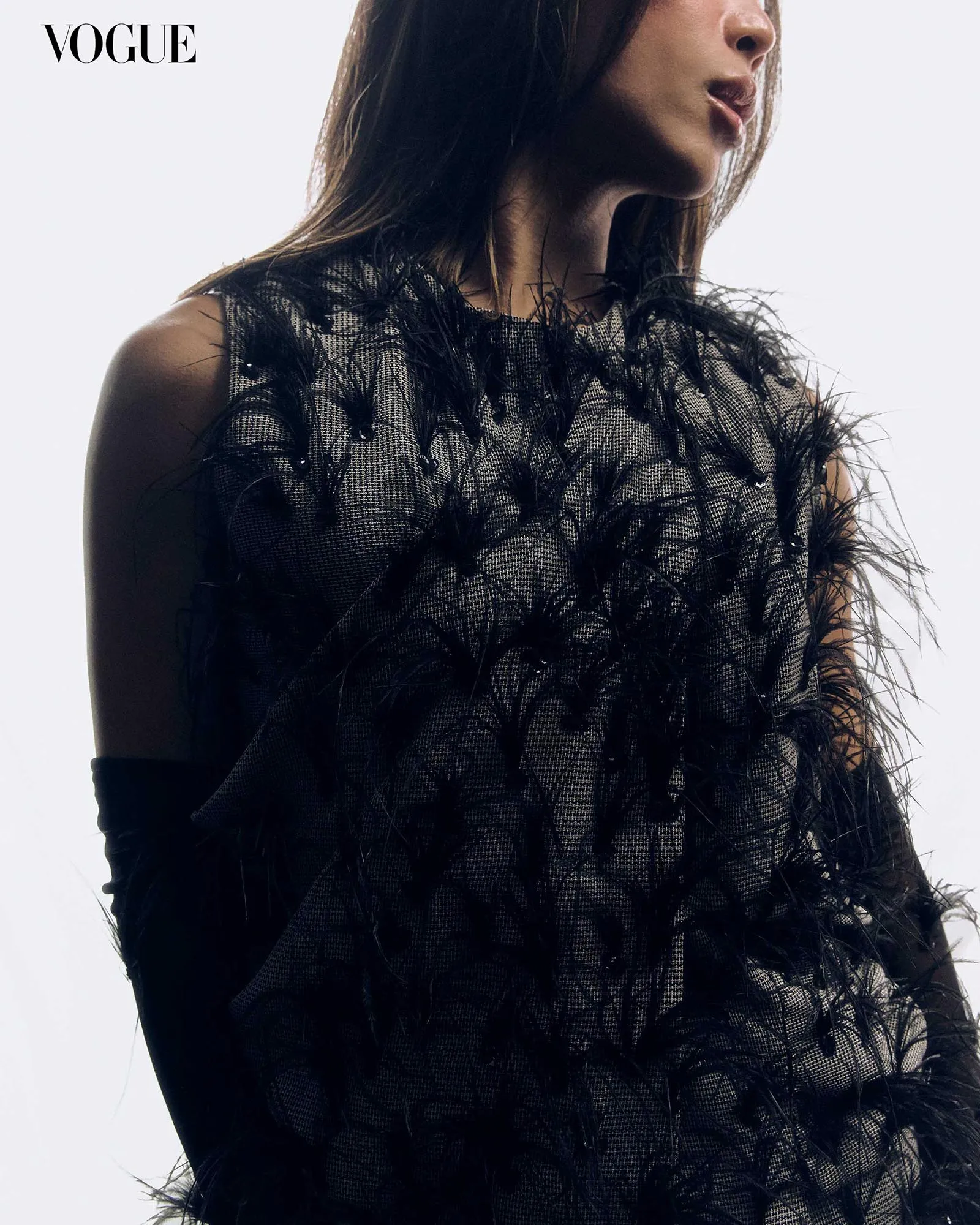 Vogue logo in the corner; a model in a black feathered dress shown in profile against a pale background.